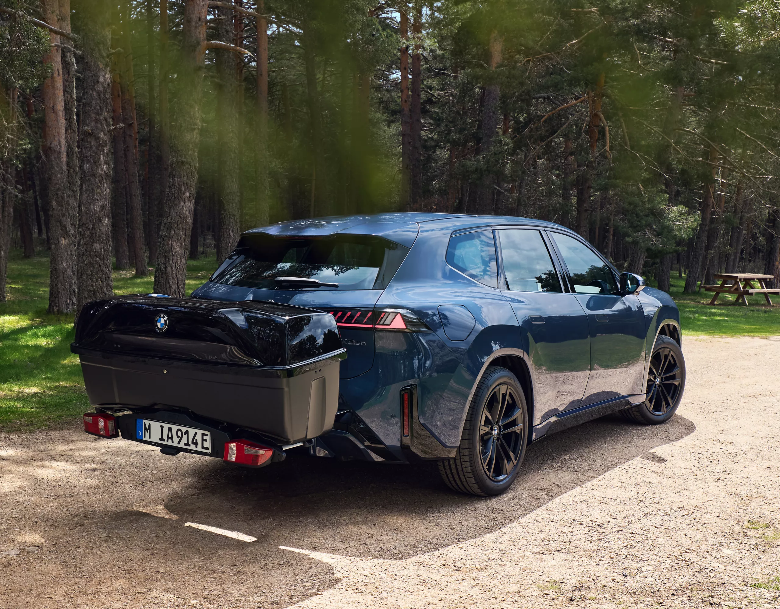 BMW Fahrzeug mit Heckträger und Transportbox steht auf einem Waldweg