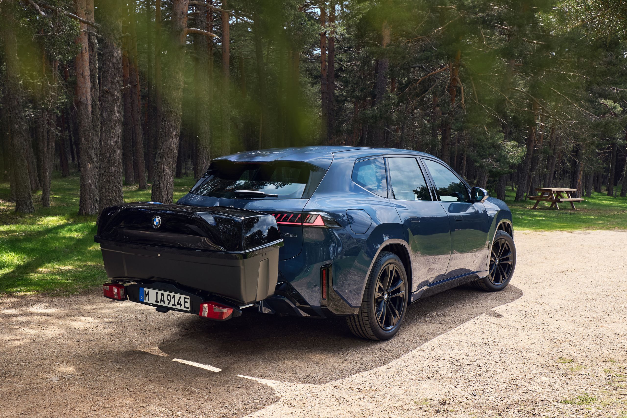 BMW Fahrzeug mit Heckträger und Transportbox steht auf einem Waldweg