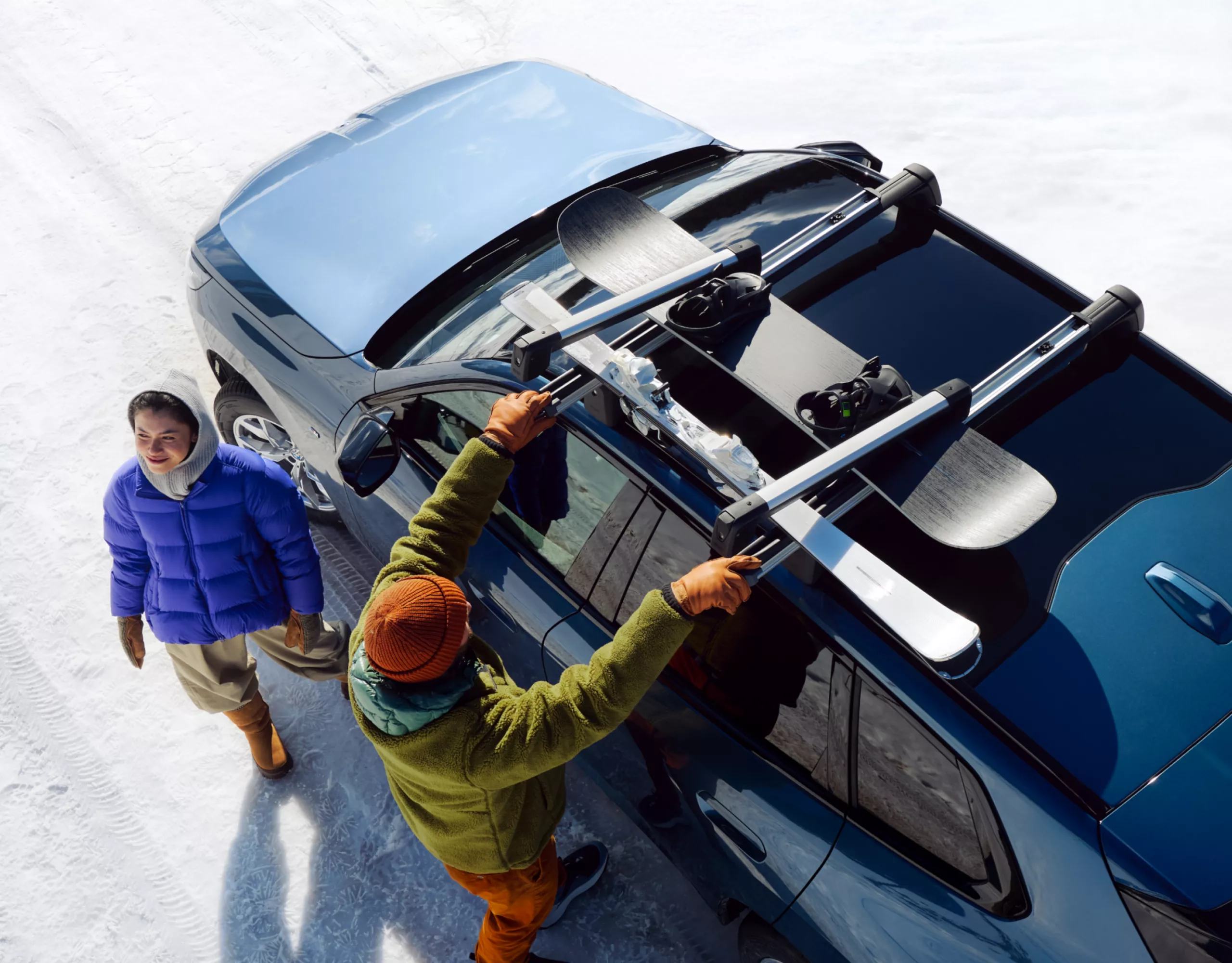 Twee mensen bevestigen ski's en een snowboard op een BMW