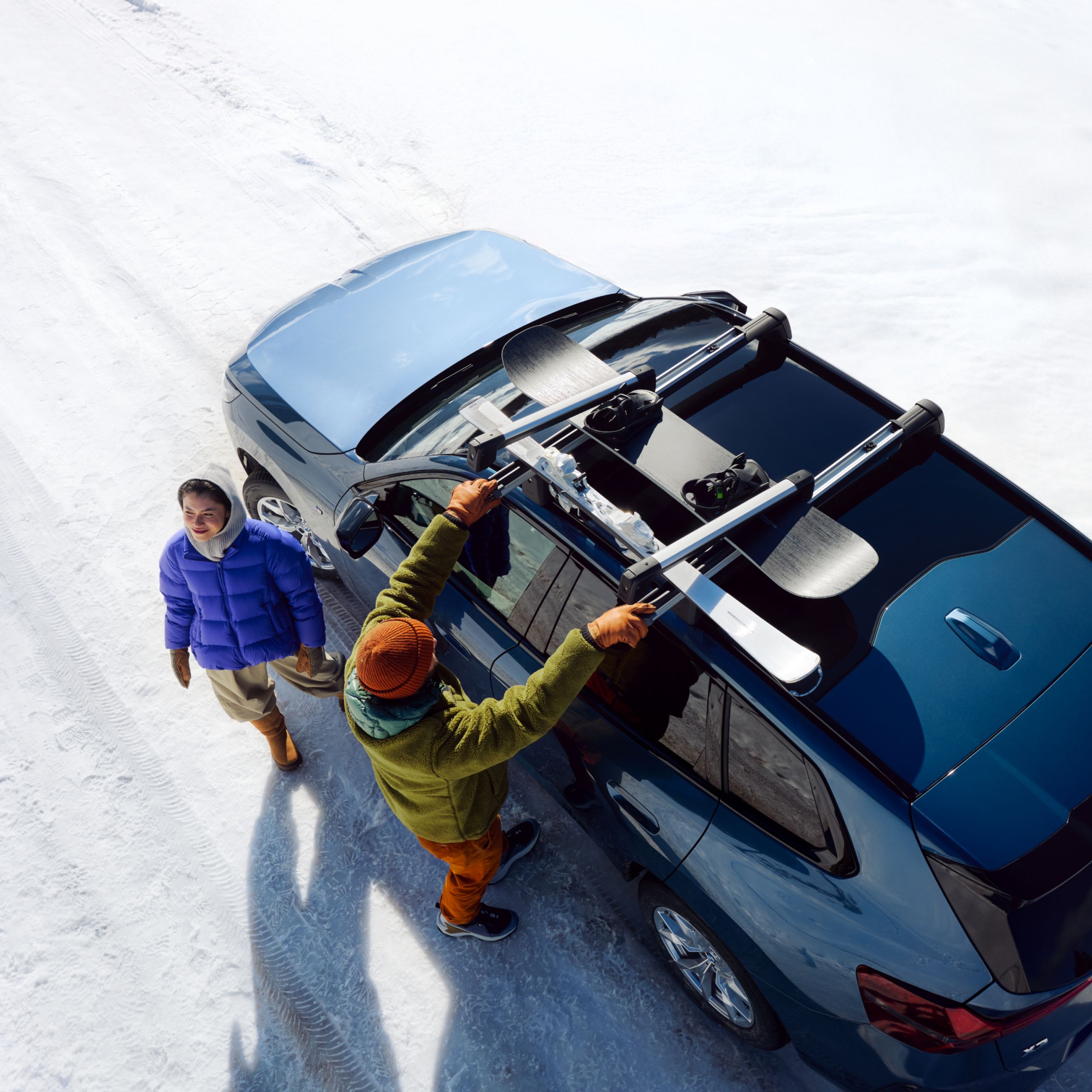 Dwie osoby mocują narty i deski snowboardowe na samochodzie BMW