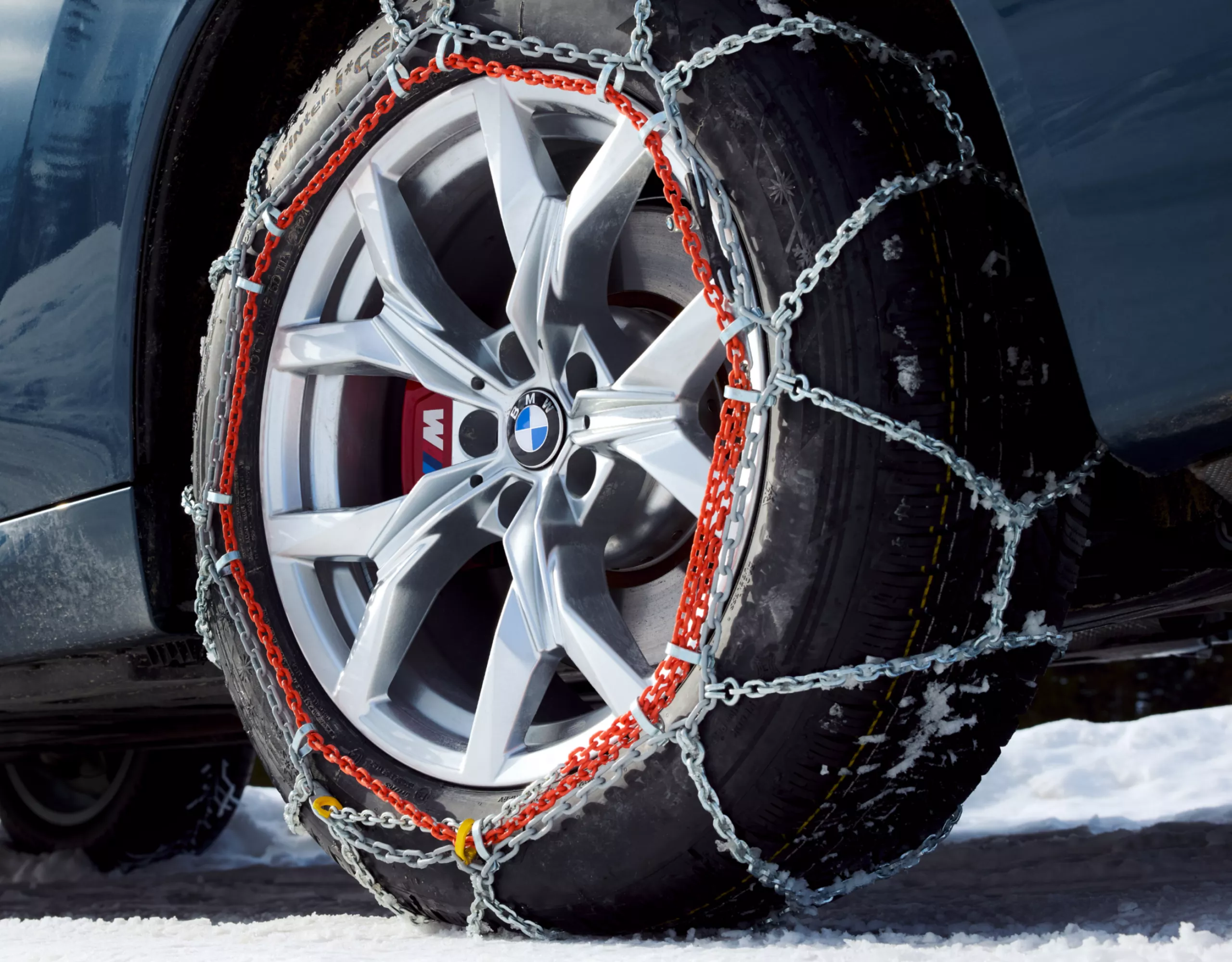 Une BMW équipée de chaînes neige est stationnée sur une route enneigée – vue détaillée de la roue arrière