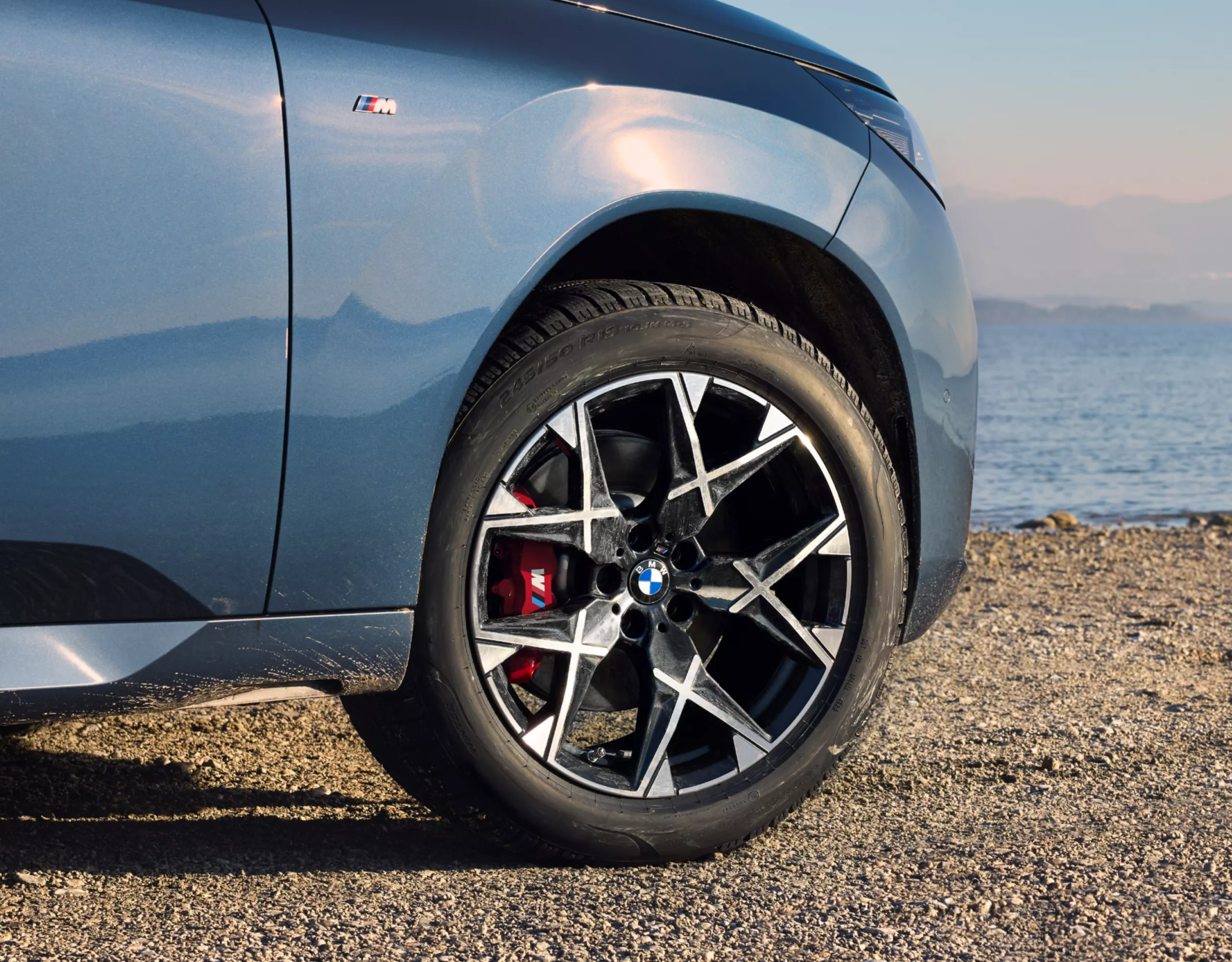 BMW steht auf steinigem Strand – Detailansicht des Winter-Komplettrads 19'' BMW Leichtmetallrad Y-Speiche 1035 M Midnight Grey, glanzgedreht