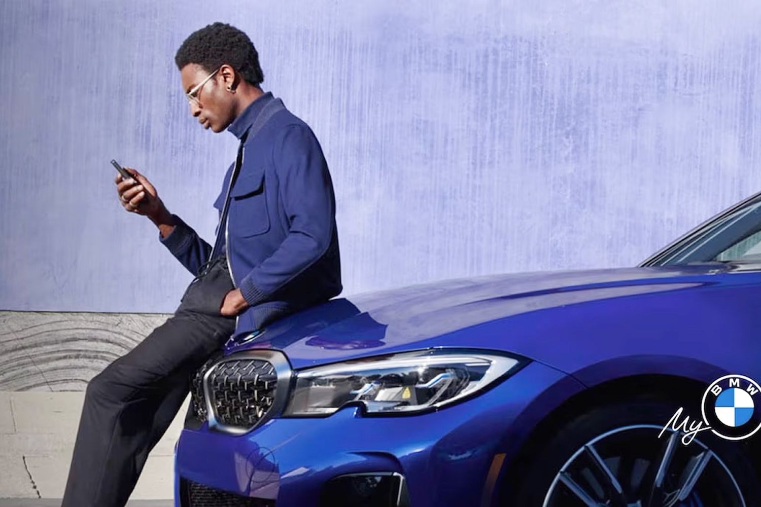 A man leans on the hood of his BMW while using his mobile phone