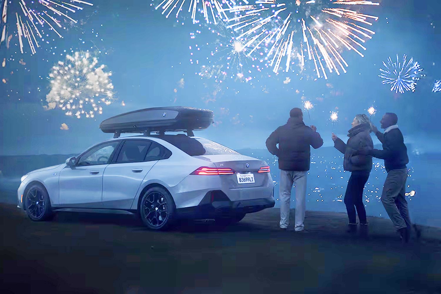 Two people watch fireworks while standing next to their BMW