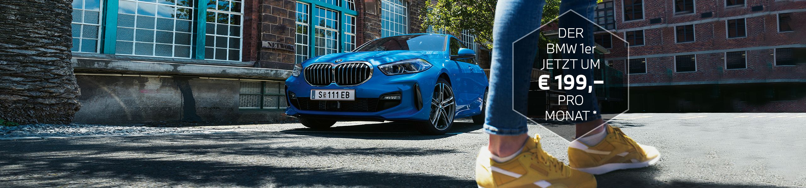 BMW 1er in blau vor historischem Gebäude und den Beinen einer Frau in Jeans und gelben Sneakers im Vordergrund.