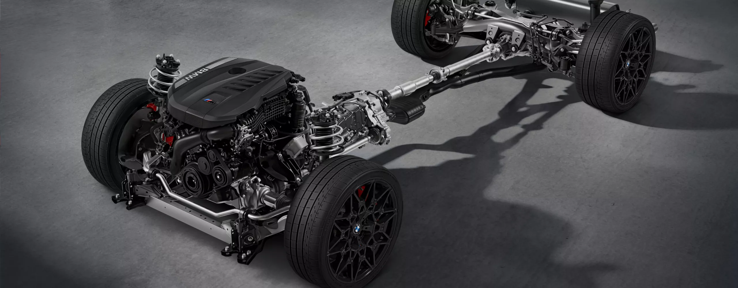 Cadena cinemática con motor de gasolina de 6 cilindros en línea BMW TwinPower Turbo, cambio y eje trasero sobre un fondo gris.