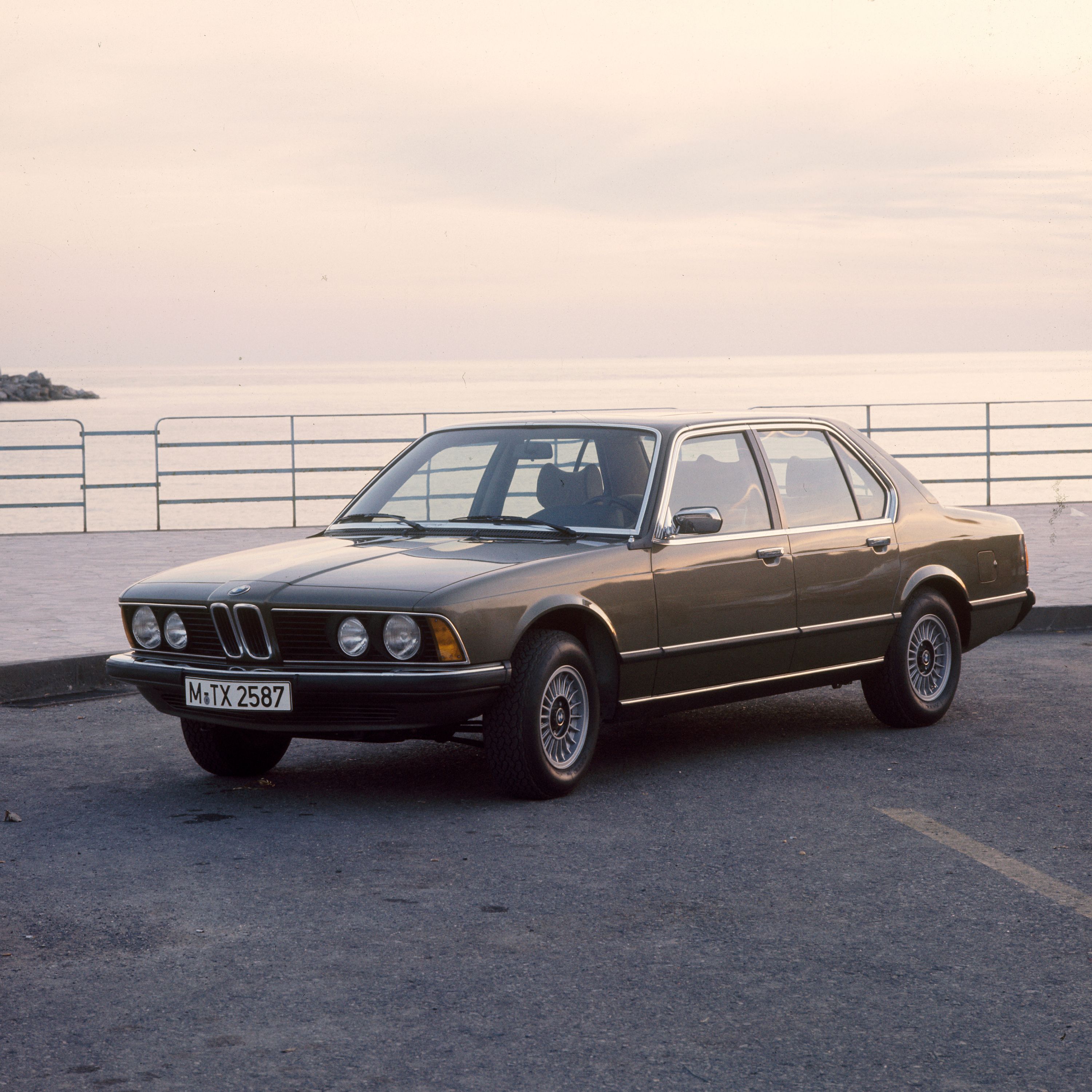 BMW Serie 7 berlina E23 parcheggiata in riva al mare con un molo di pietra sullo sfondo