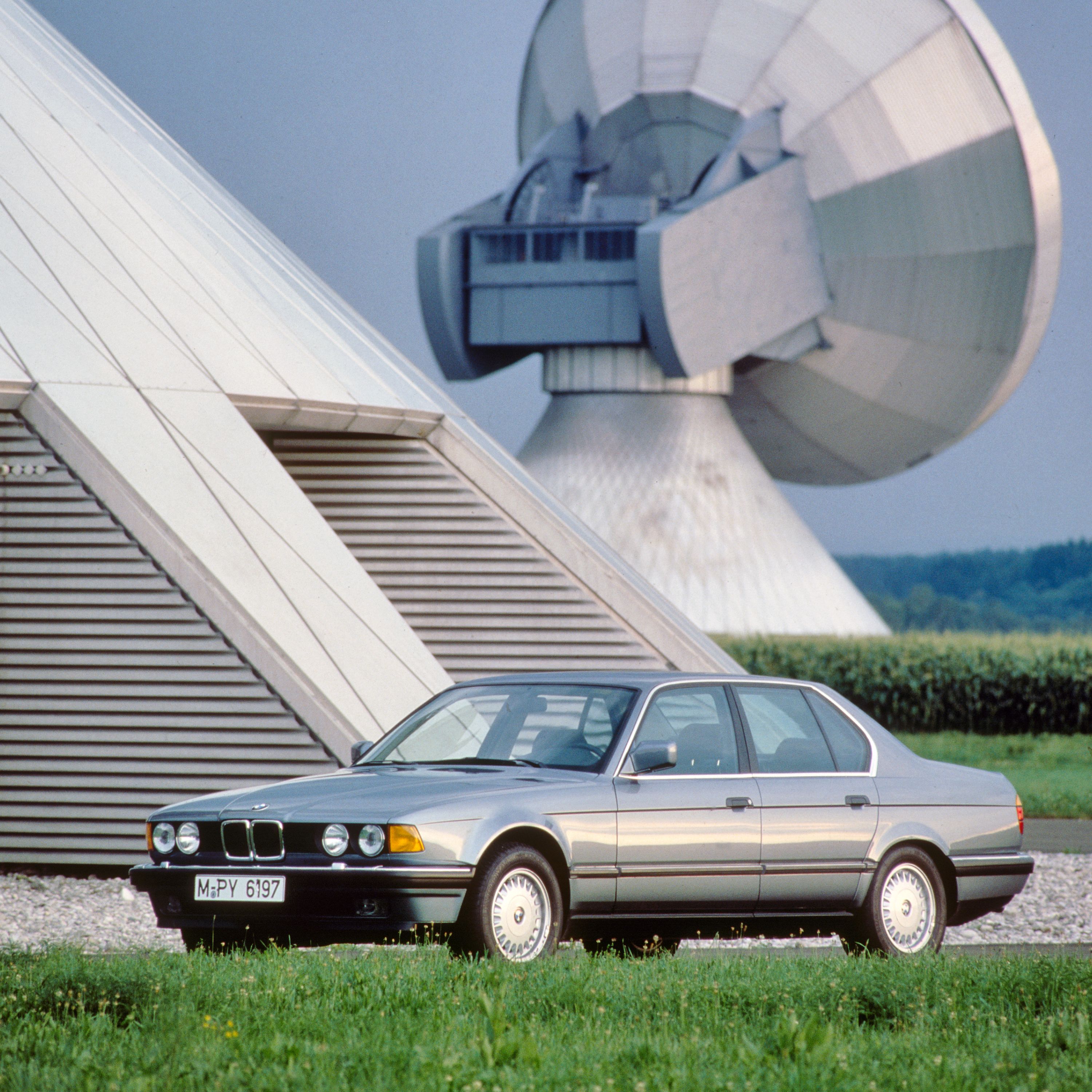 BMW Série 7 Berline E32 dans un environnement agricole entouré de champs et d'installations agricoles