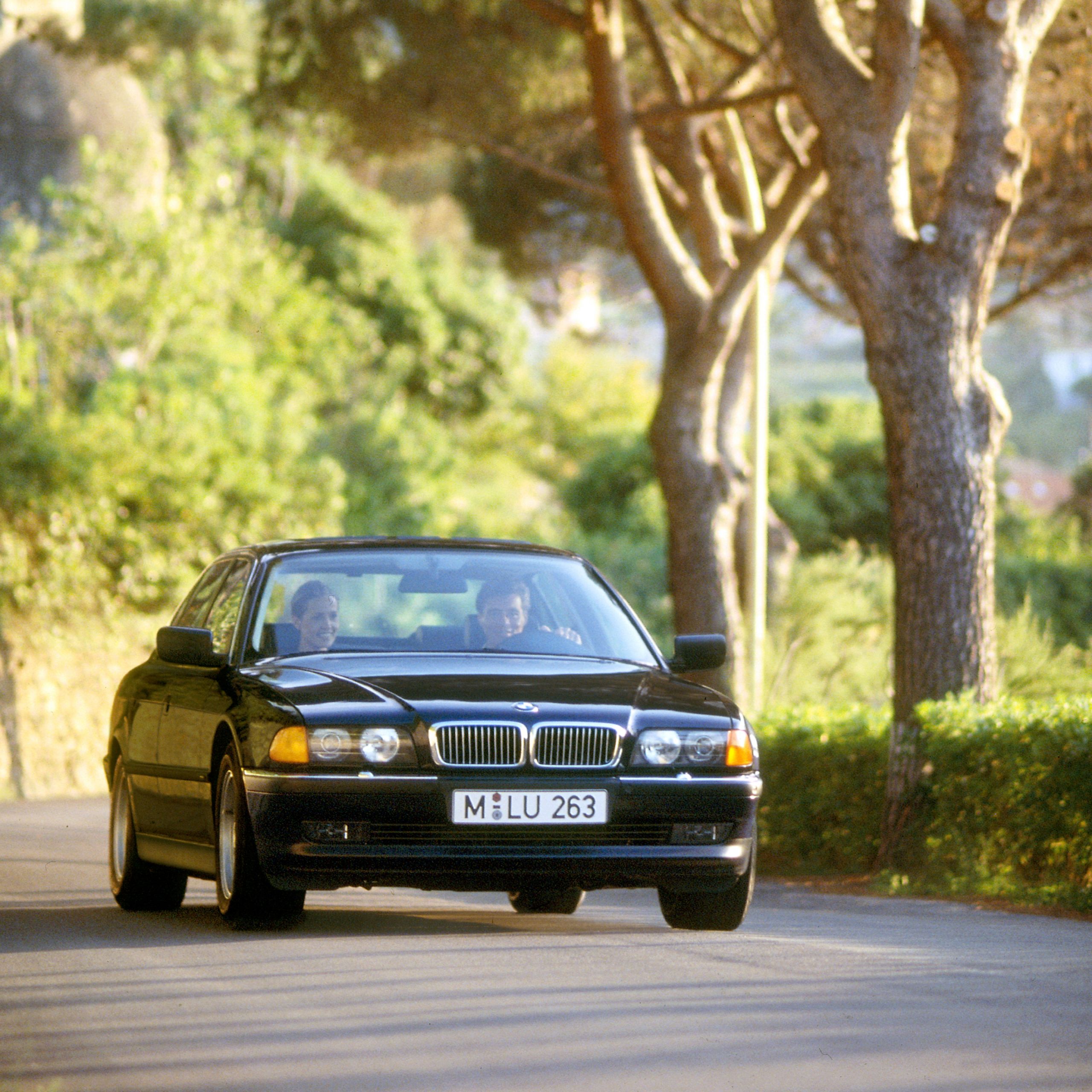 BMW 7 Serie Sedan E38 op een landweg in de zomer met een dorp op de achtergrond