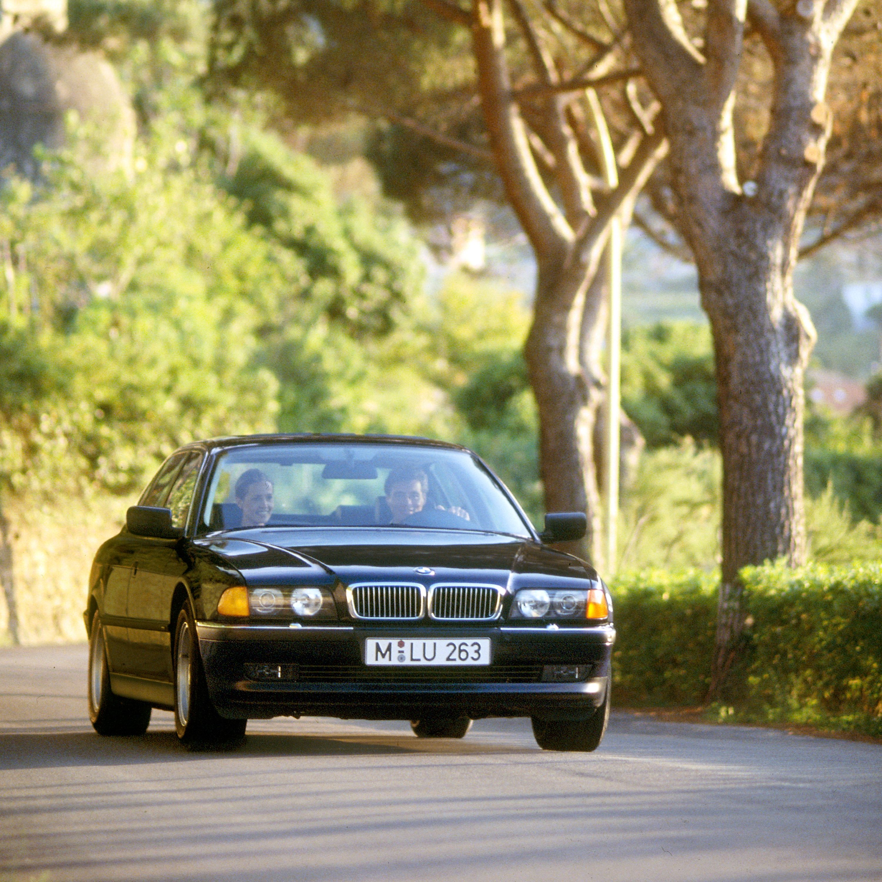 BMW 7er Limousine E38 auf einer Alleenstraße in ländlicher Umgebung im Sommer mit einem Dorf im Hintergrund