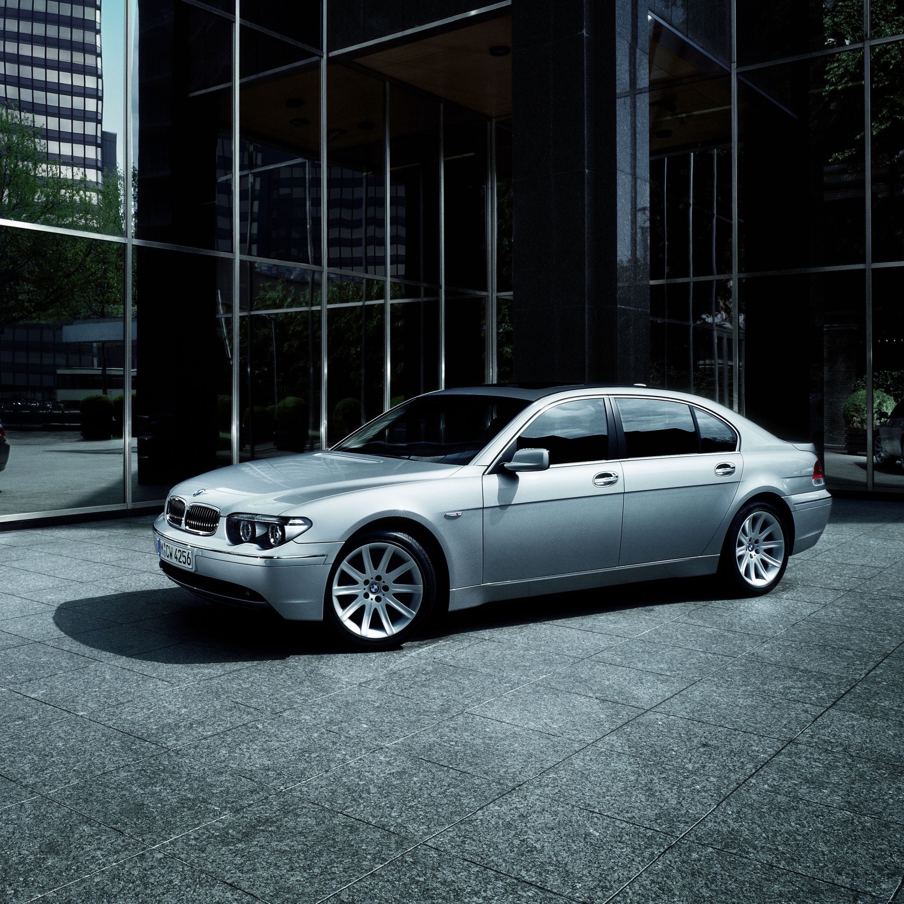 BMW 7 Series Sedan E65, E66, E67, E68 parked in front of a modern high-rise building with a black tinted glass front
