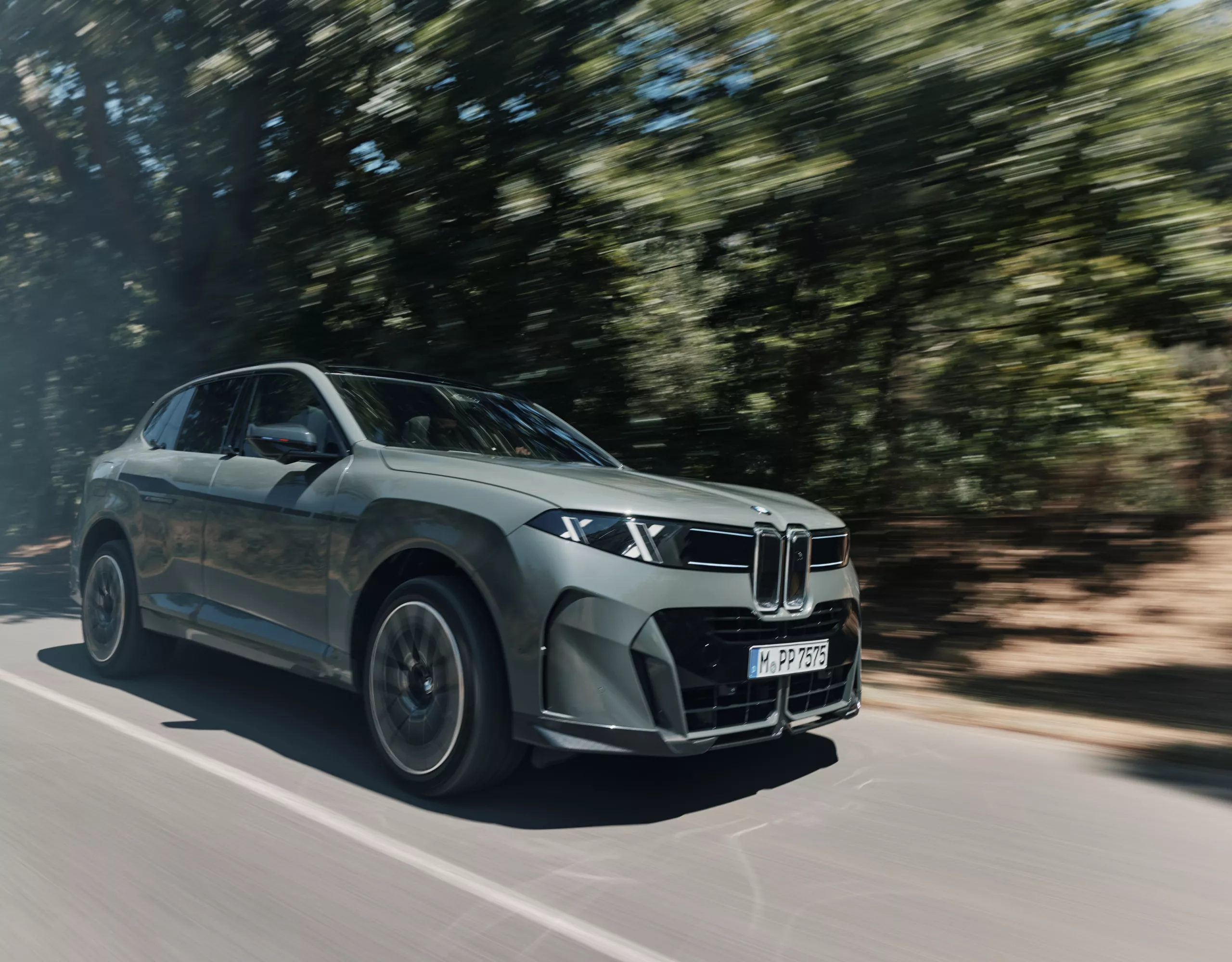 La BMW iX5 roule sur une route de campagne à travers la forêt