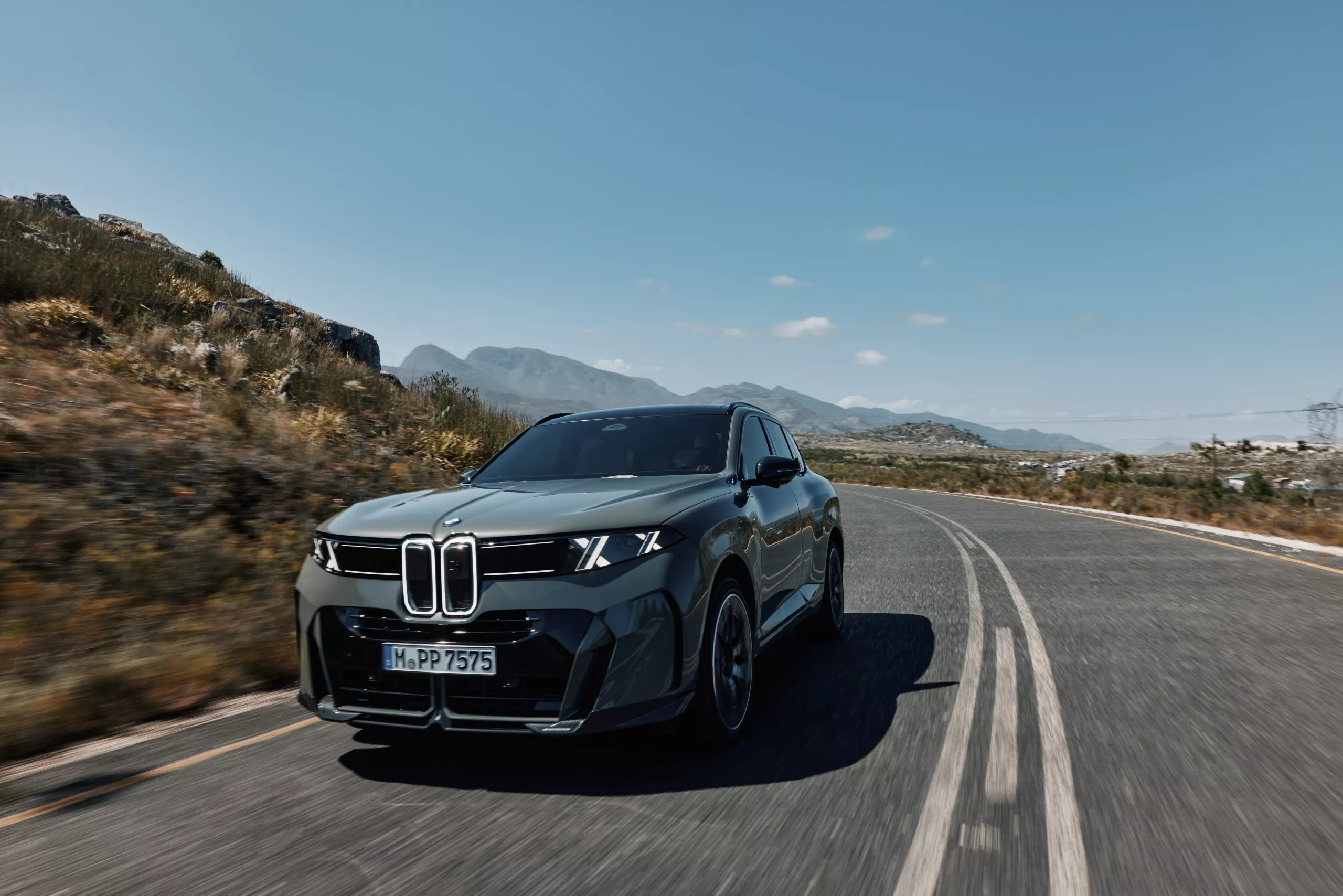 Η BMW iX5 κινείται σε ελικοειδή ορεινό δρόμο κατά το ηλιοβασίλεμα