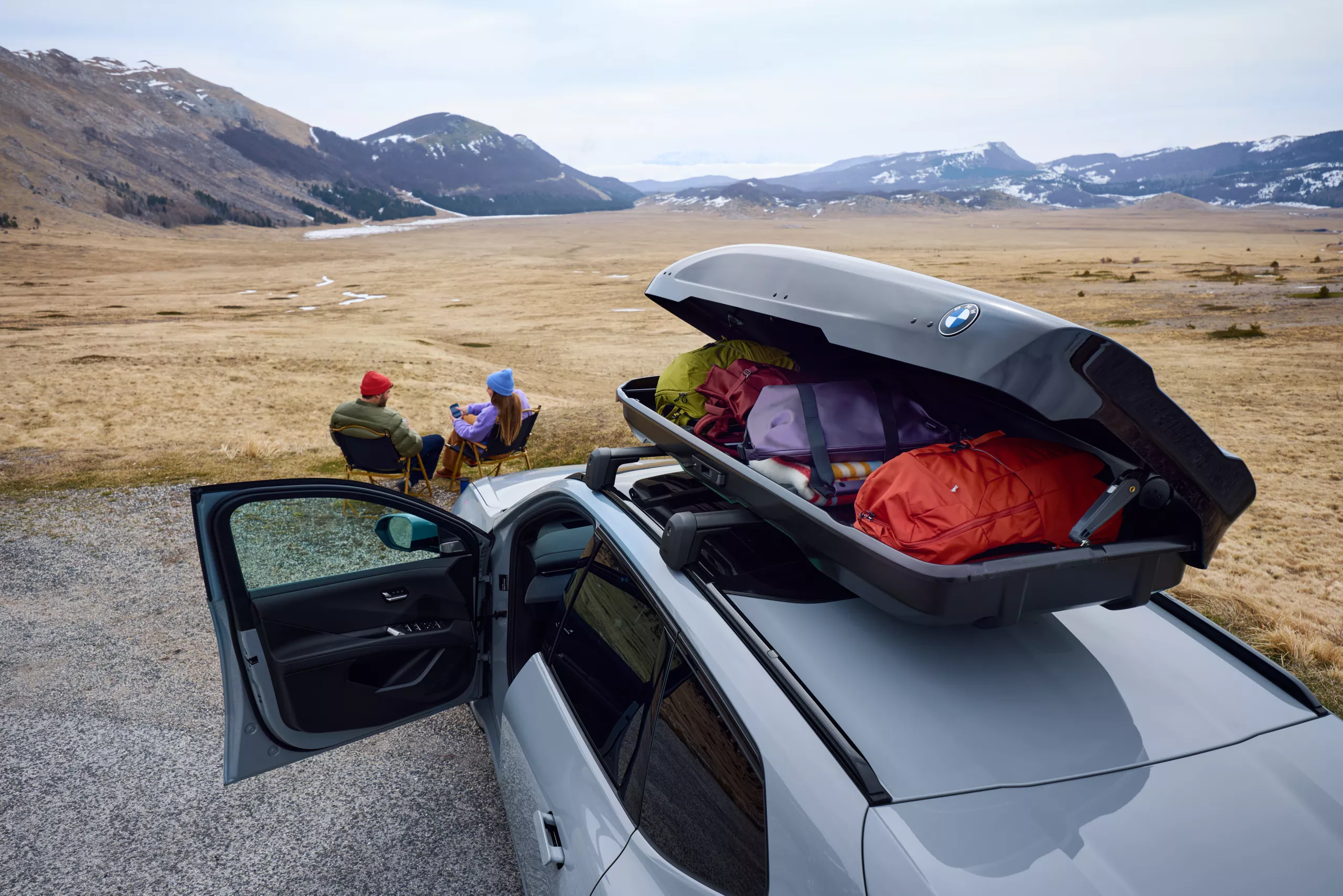 Open original BMW roof box loaded with luggage, couple camping in mountain landscape in background