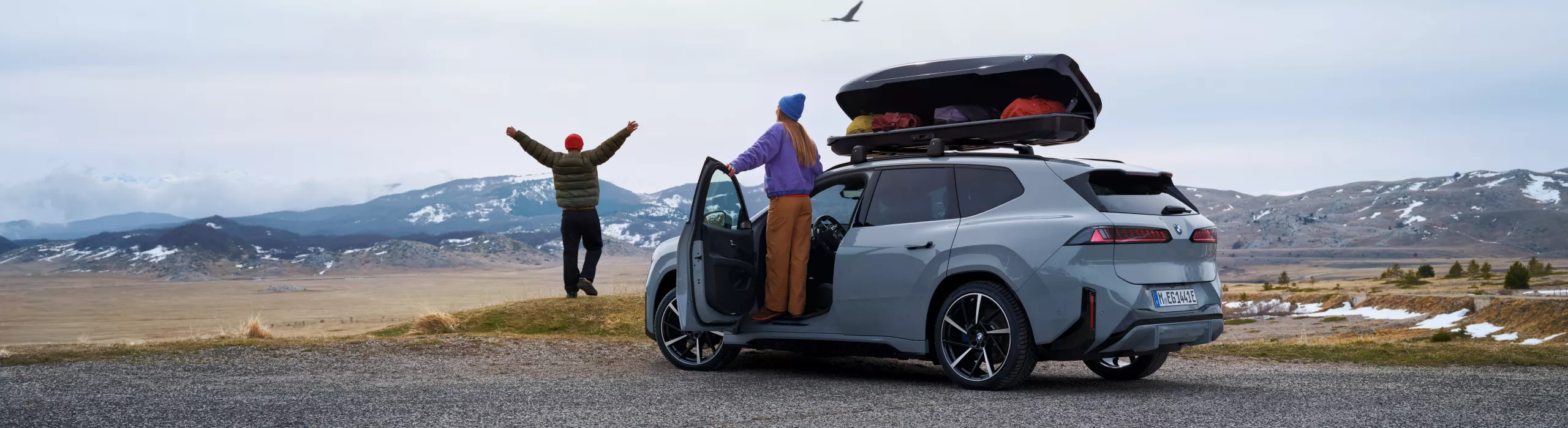 BMW SUV tetőcsomagtartóval hegyvidéki tájban, az előtérben emberek