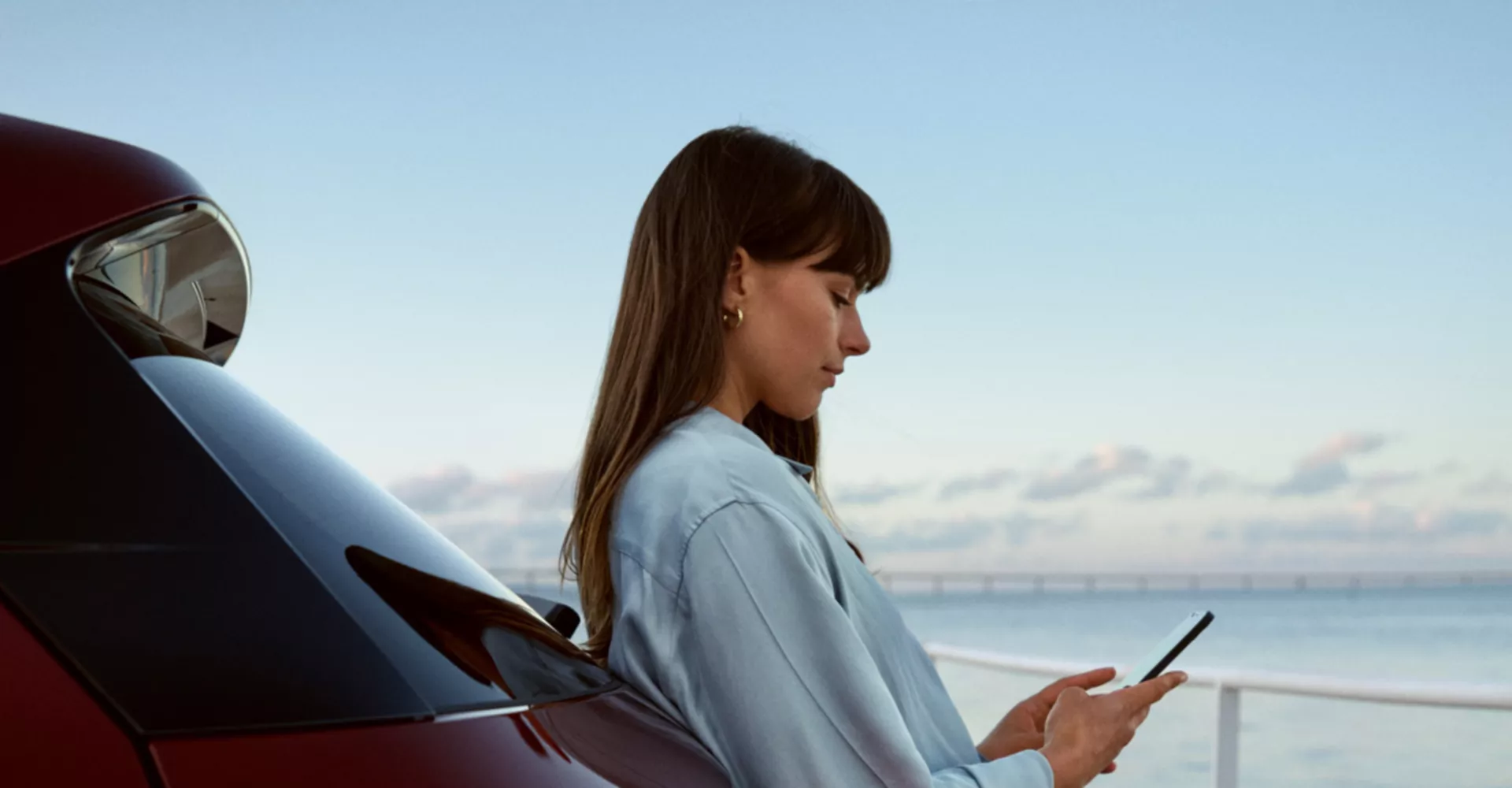 Mulher encostada a um BMW, a usar o telemóvel junto ao mar 