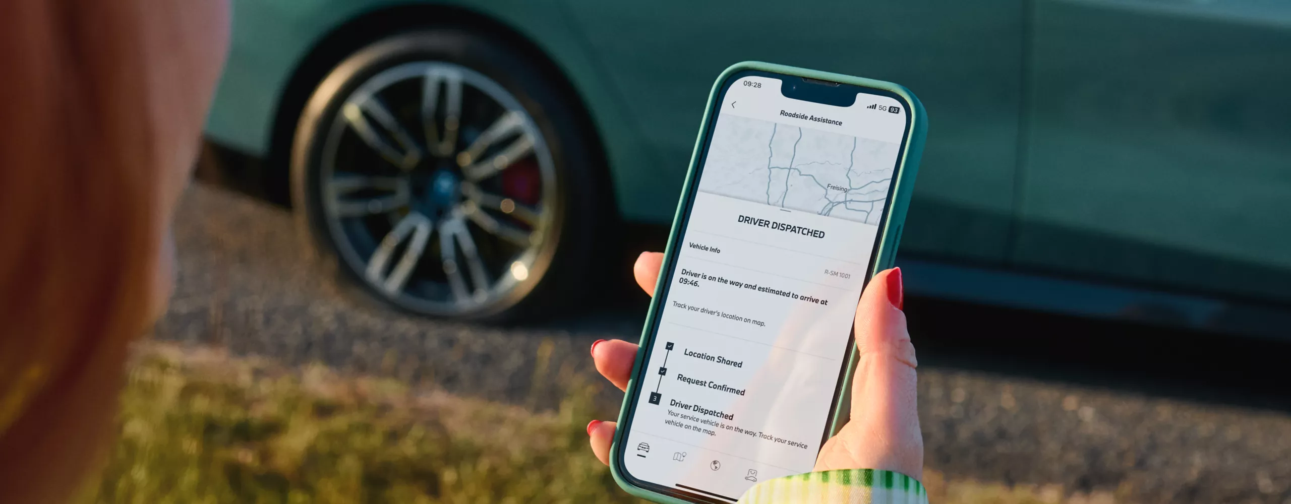 The picture shows a person standing next to a BMW, using their smartphone to contact the BMW breakdown and accident service.