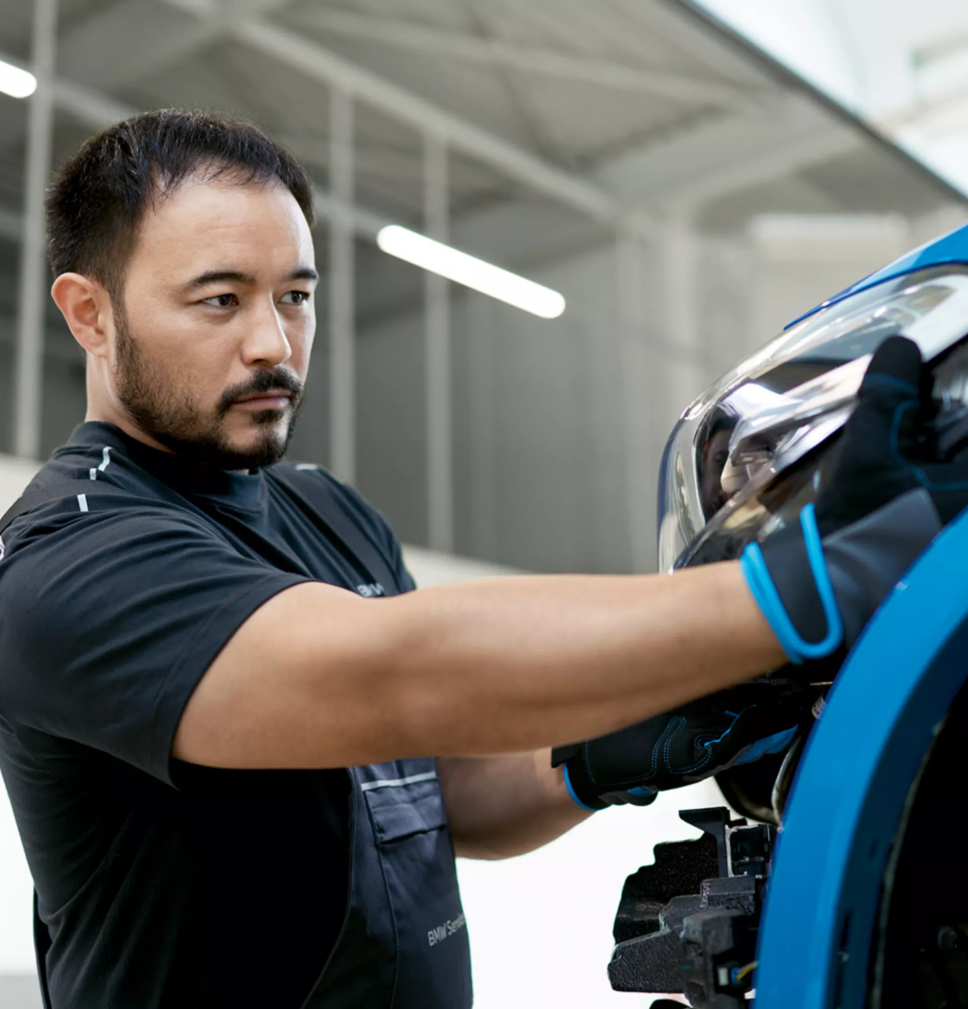 Un uomo installa un proiettore in una BMW blu all’interno di uno stabilimento produttivo