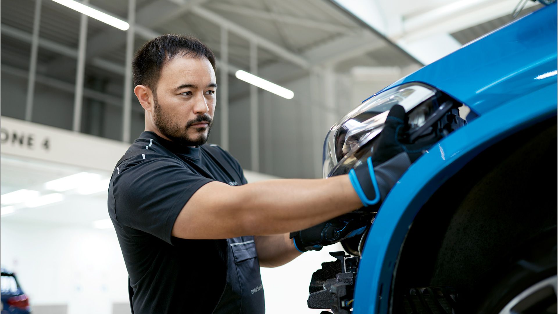 Un uomo installa un proiettore in una BMW blu all’interno di uno stabilimento produttivo