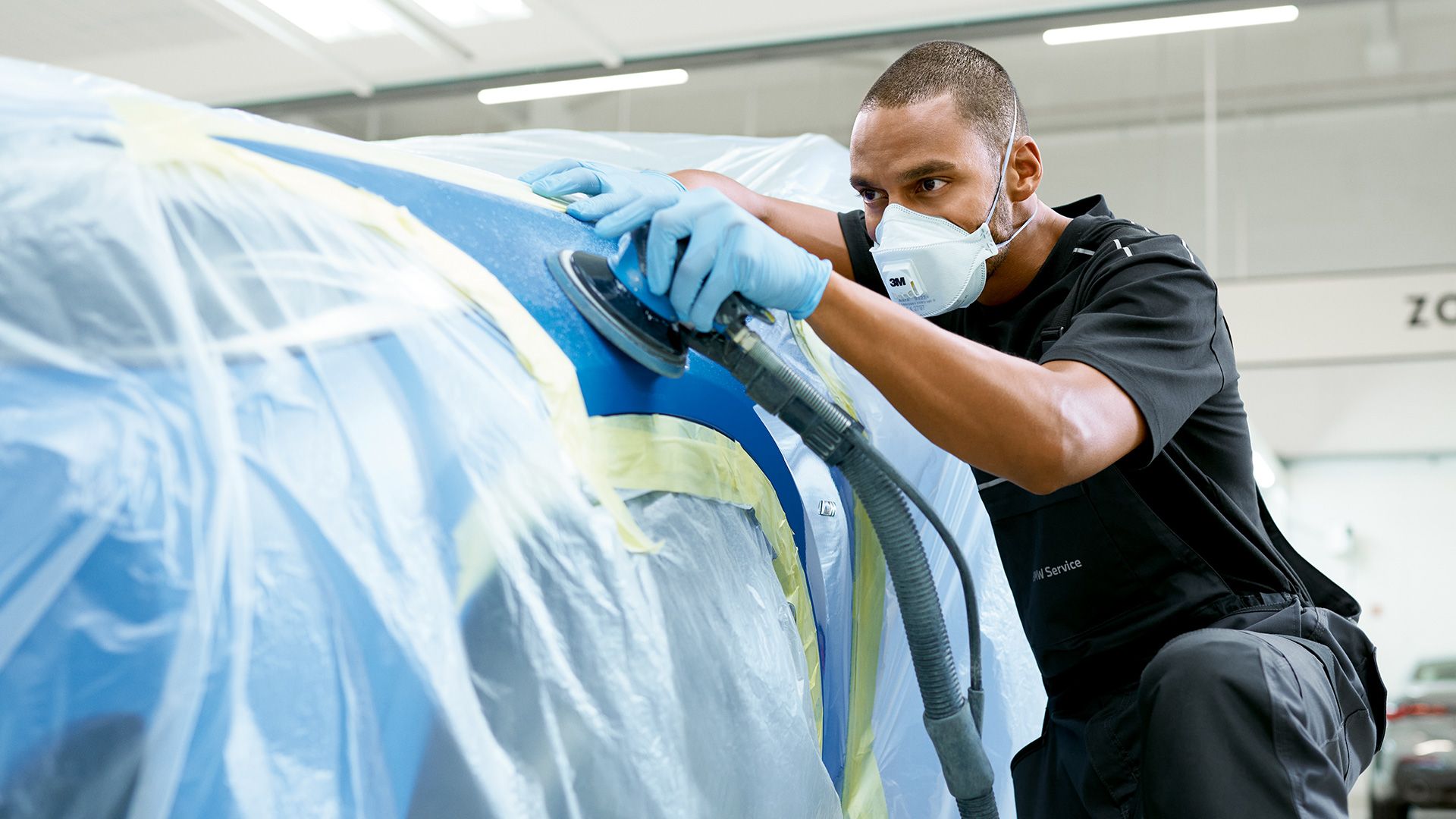 Un uomo con una mascherina lavora sul copriruota anteriore di una BMW con una lucidatrice