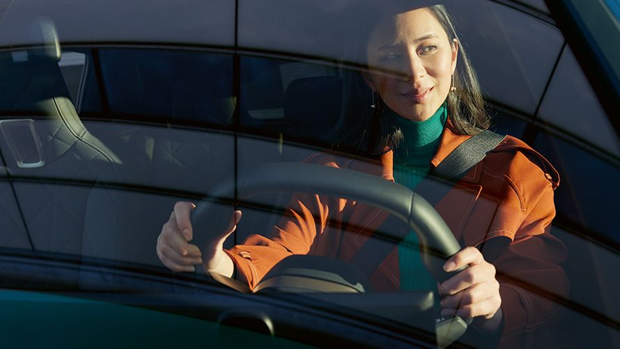 Una donna con una giacca arancione è seduta al posto di guida di una BMW