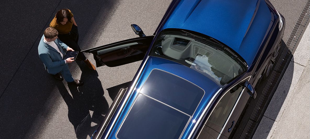 Un consulente BMW con un tablet in mano si trova con una cliente di fronte alla portiera aperta di una BMW con prospettiva a volo di uccello