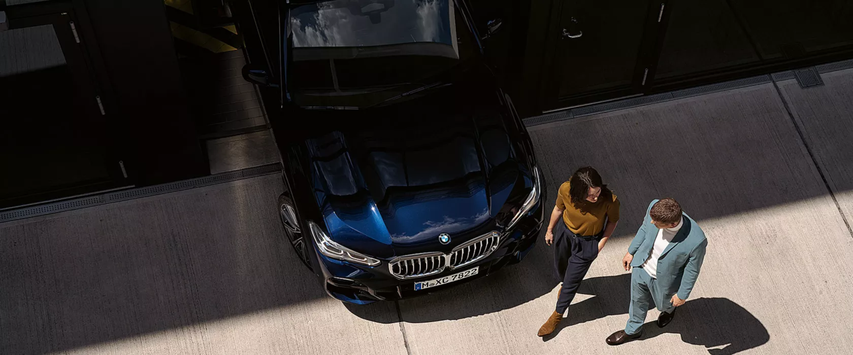 Woman and man walk past the front of the BMW