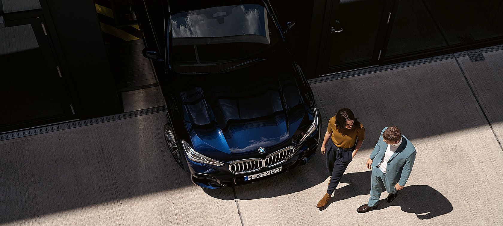 Mulher e homem a caminhar perto da dianteira de um BMW a partir de uma perspetiva aérea