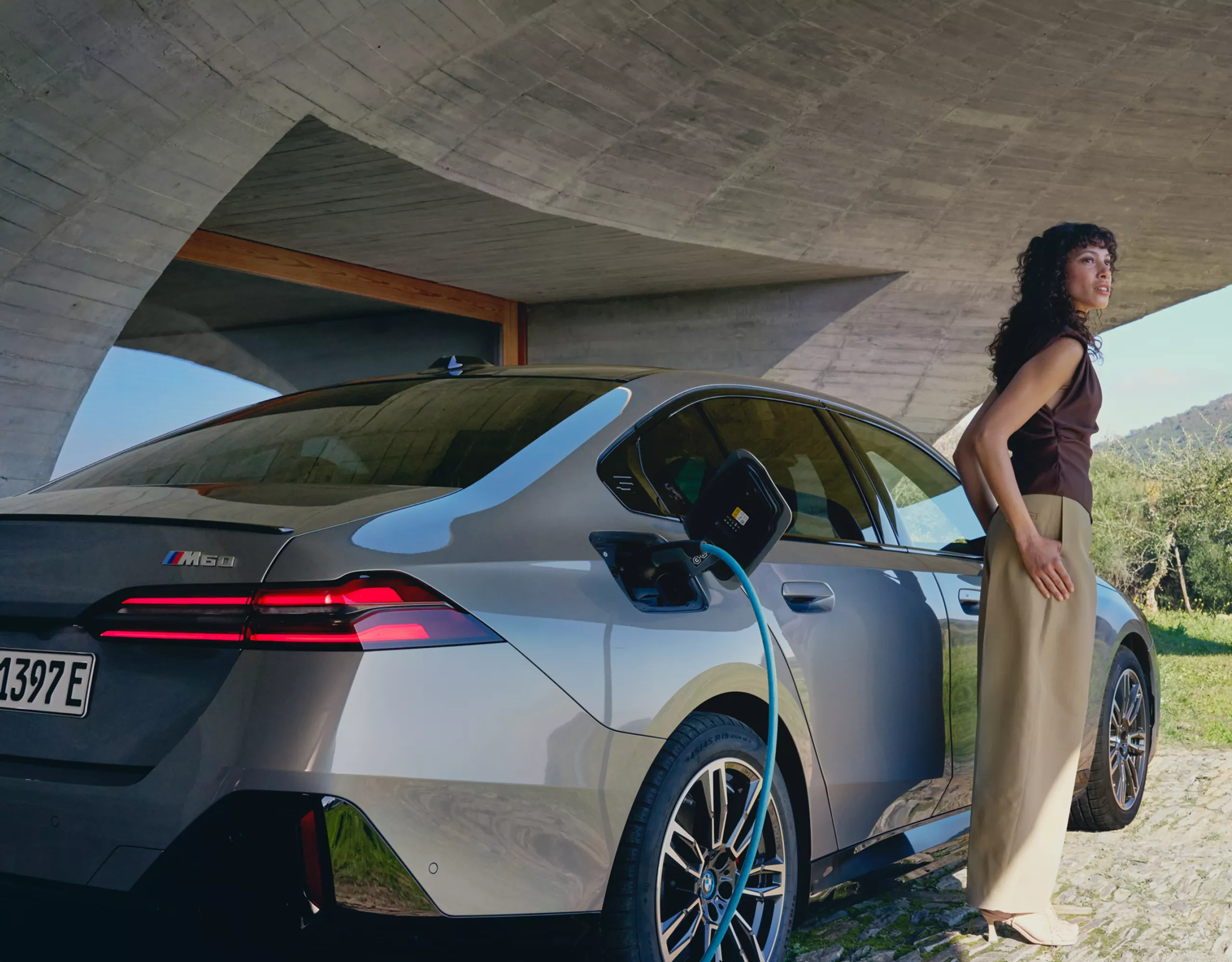 Ein graues BMW Elektrofahrzeug wird geladen. Daneben steht eine Frau.