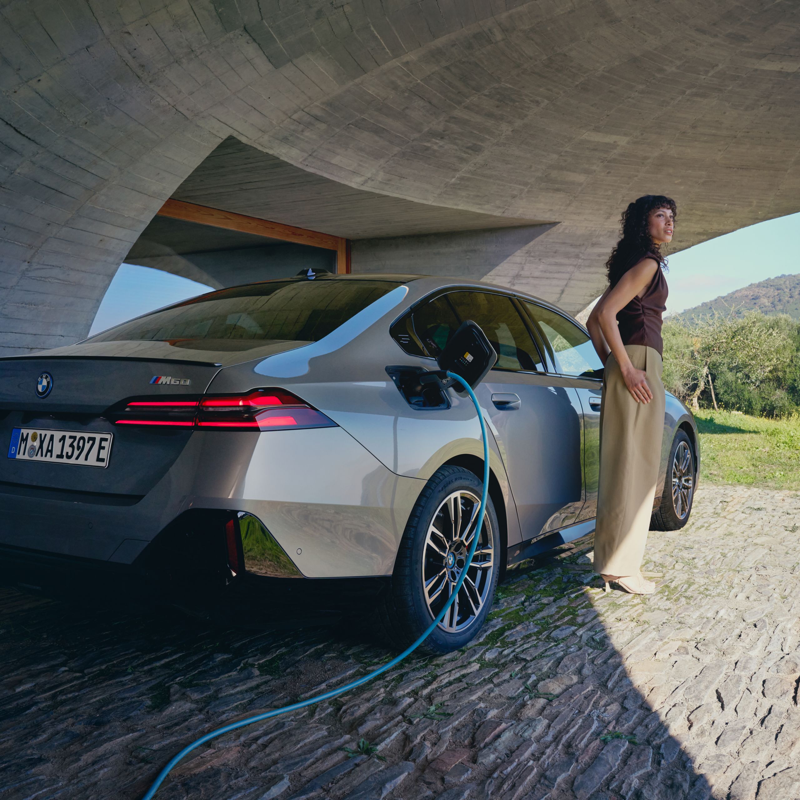Ein graues BMW Elektrofahrzeug wird geladen. Daneben steht eine Frau.