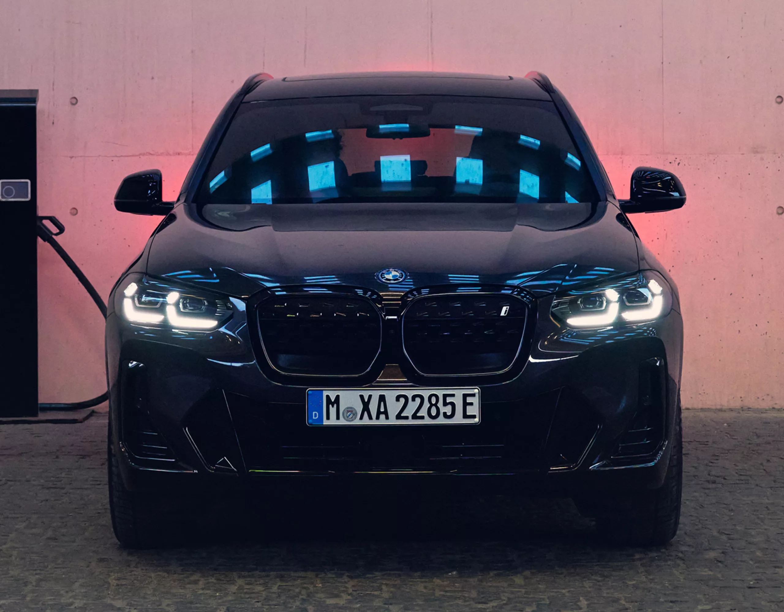 Vue frontale d’une BMW noire. La BMW est garée à côté d’une borne de recharge.