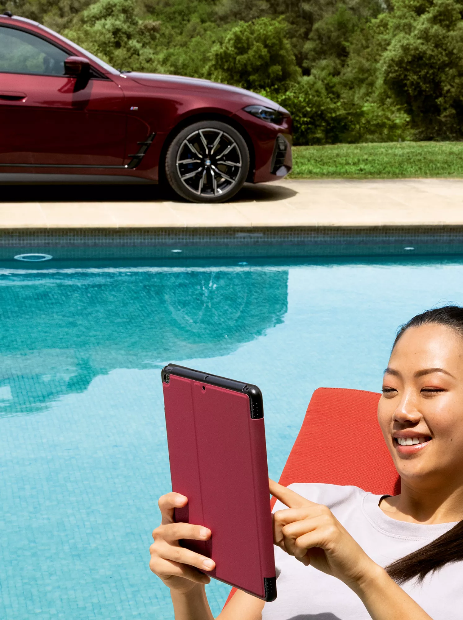 Une femme allongée sur une chaise longue au bord de la piscine regarde sa tablette. 