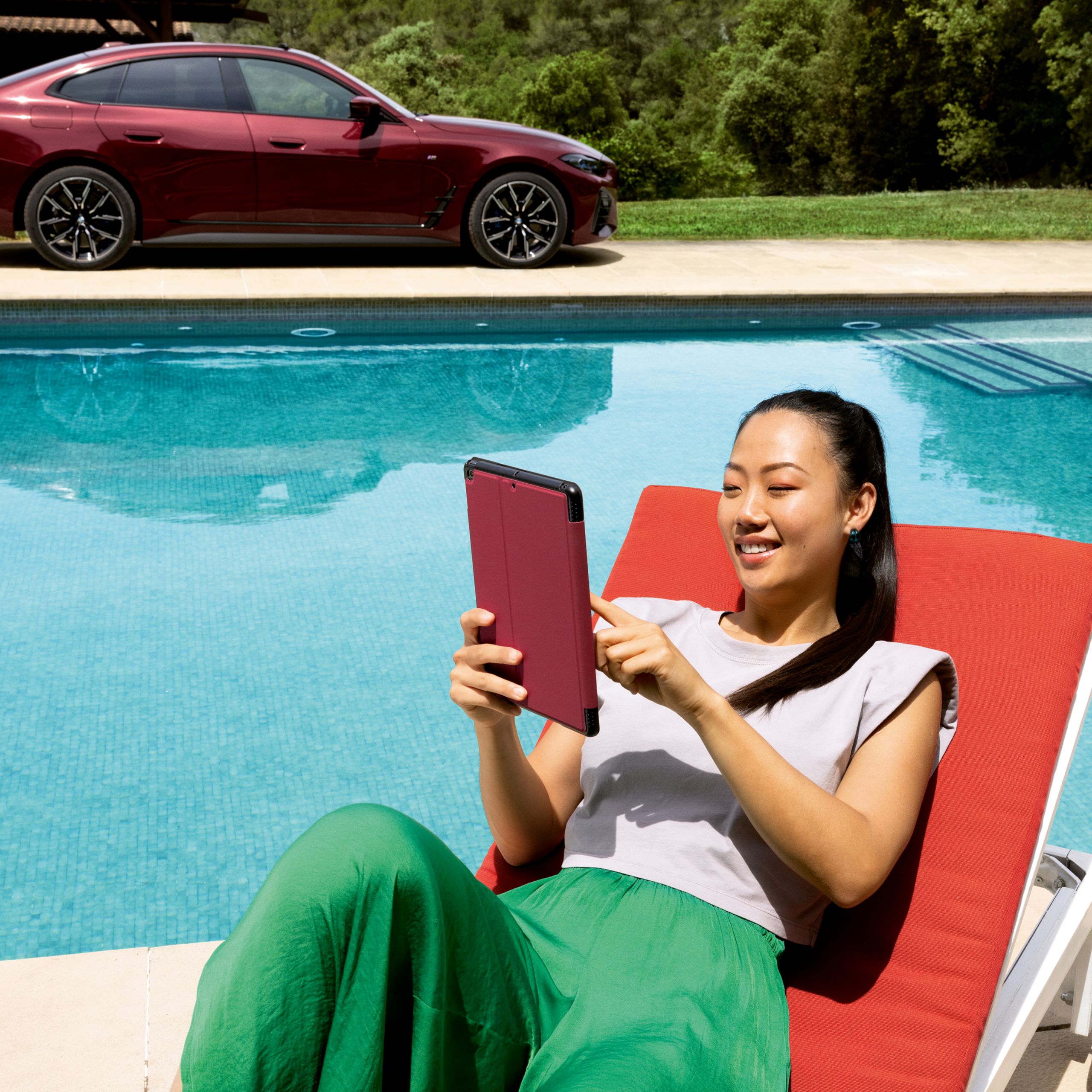 Eine Frau liegt auf einem Liegestuhl am Pool und schaut in ihr Tablet.