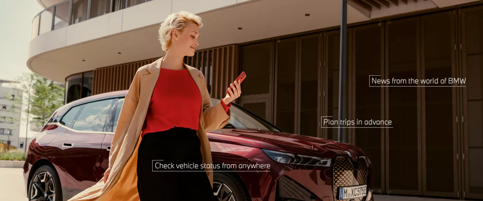 Woman in front of BWW iX uses My BMW app on smartphone