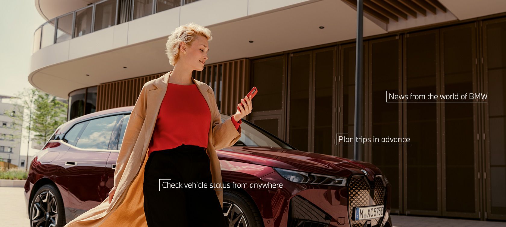 Woman in front of BWW iX uses My BMW app on smartphone