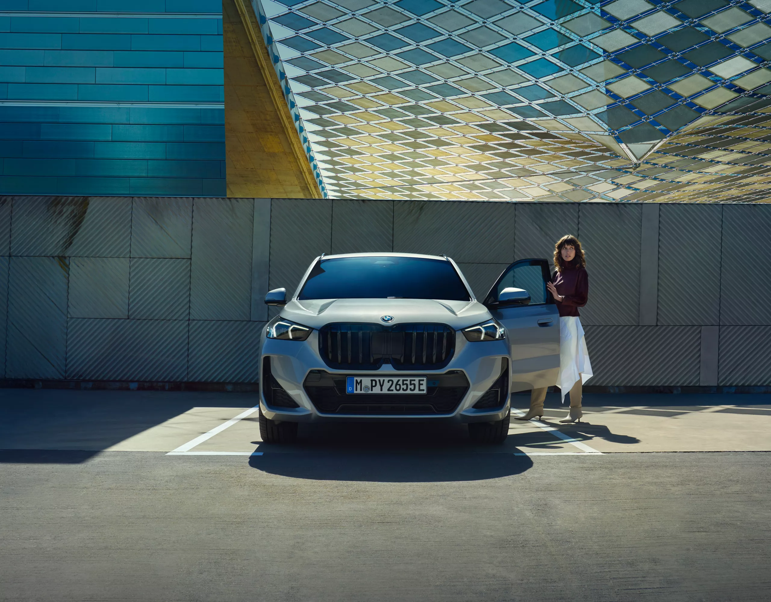 Profissional de negócios a afastar-se de um veículo de empresa BMW iX3 azul estacionado em frente à fachada metálica moderna de um edifício