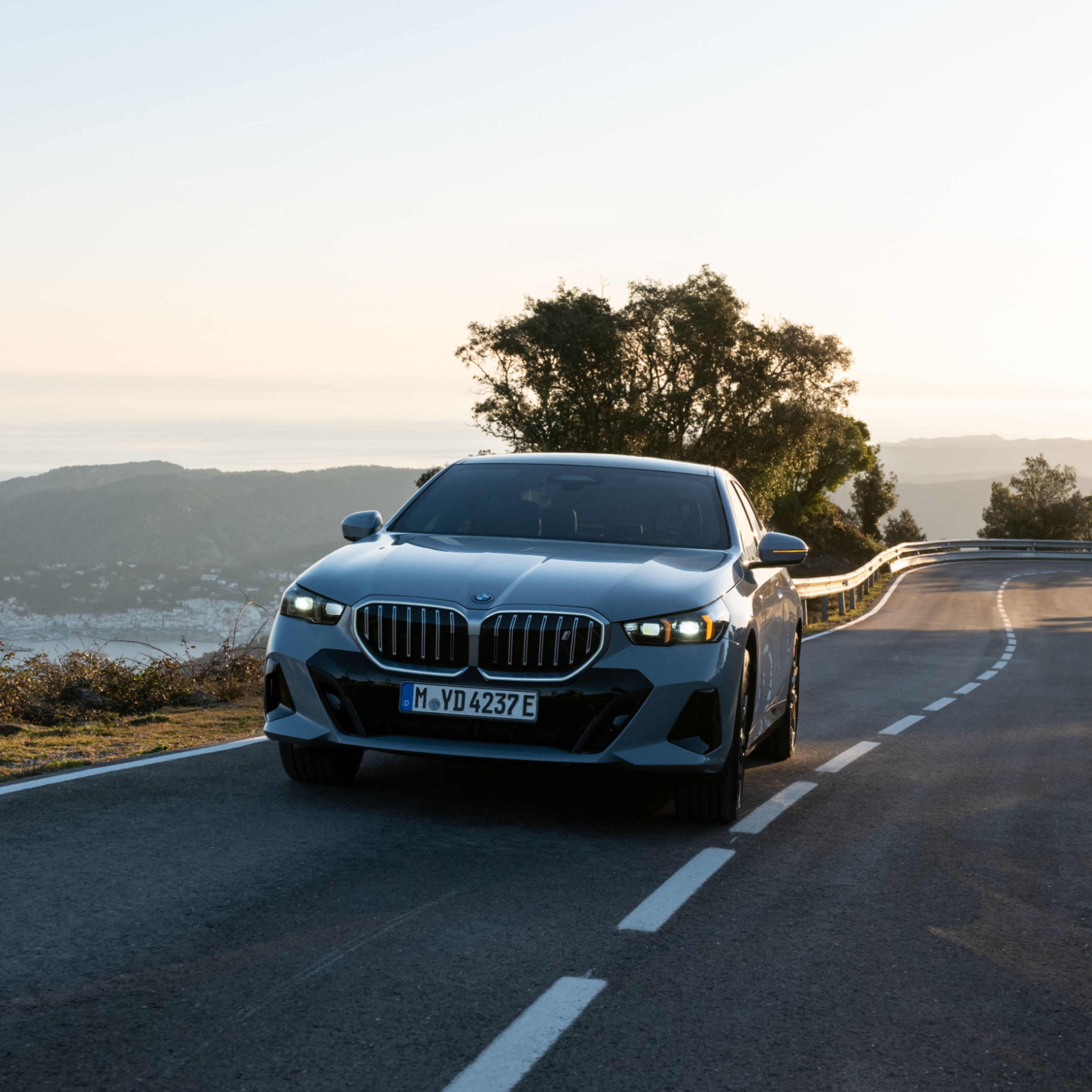 BMW i5 Sedan σε γκρι Frozen Pure μεταλλικό, σε παραλιακό δρόμο σε μεσογειακό σκηνικό