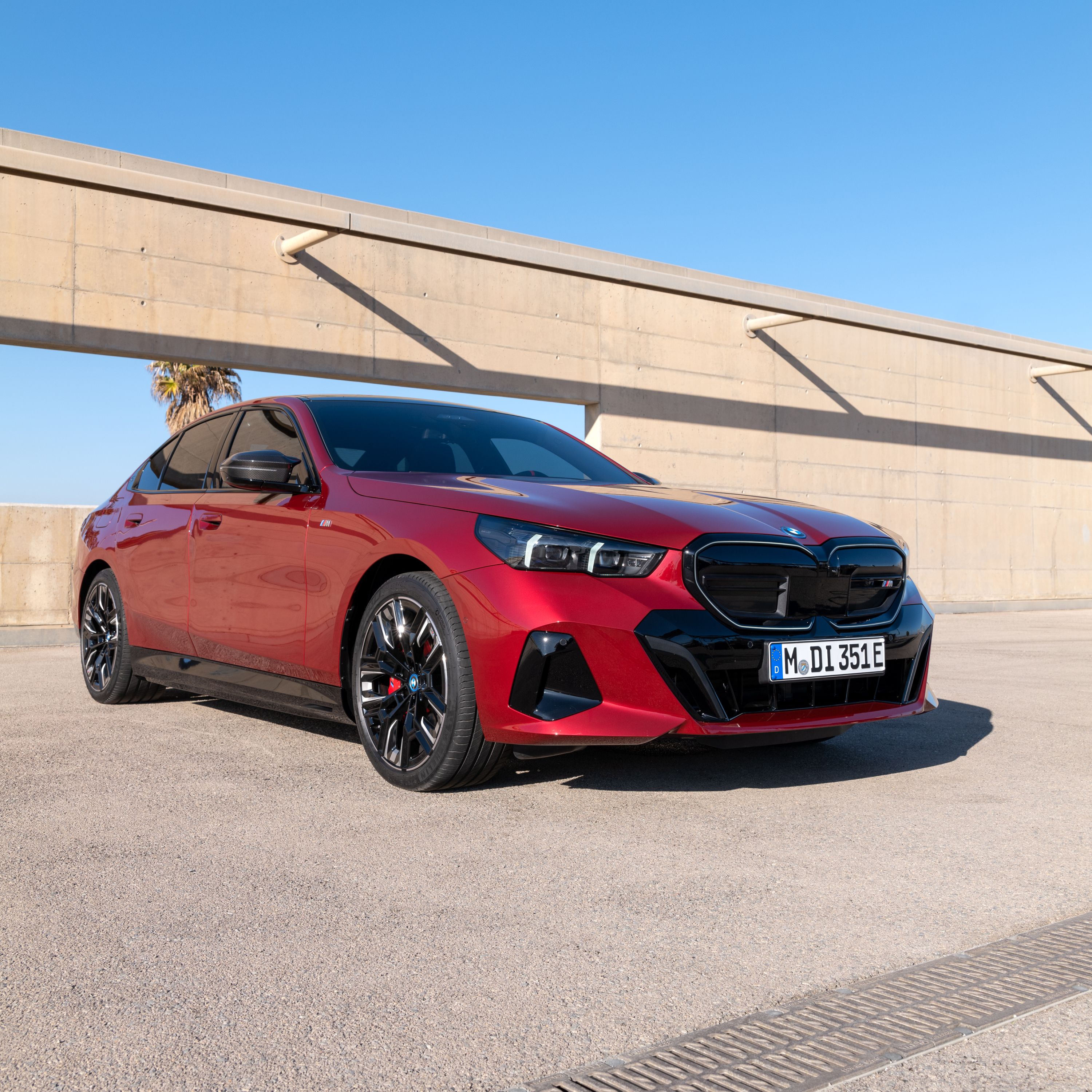 BMW i5 Sedan M60 xDrive in Fire Red Metallic, parked on the roof of a brightly coloured parking garage