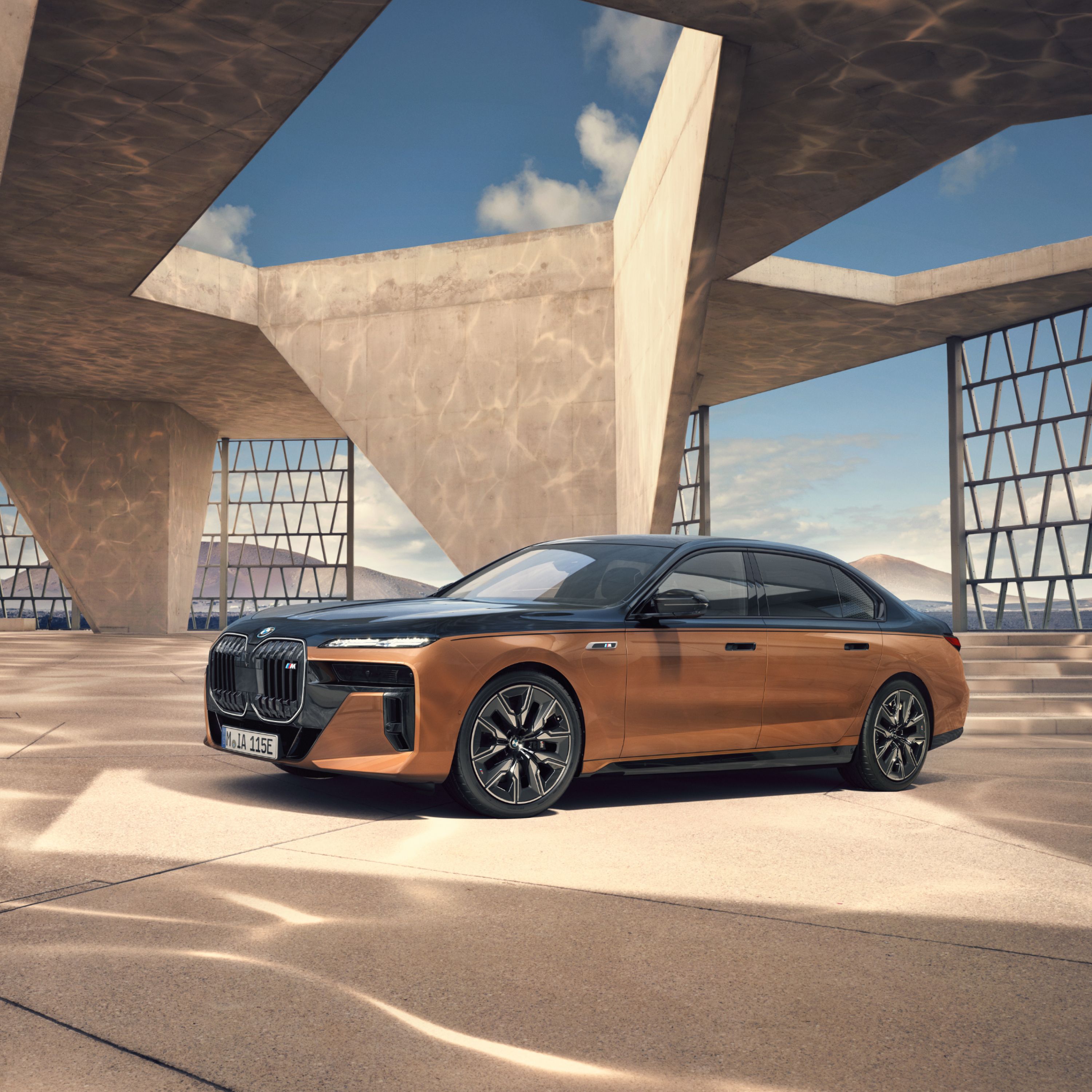 BMW i7 M70 xDrive Sedan in Individual Two-Tone paint in a modern architectural construction with a mountain panorama in the background