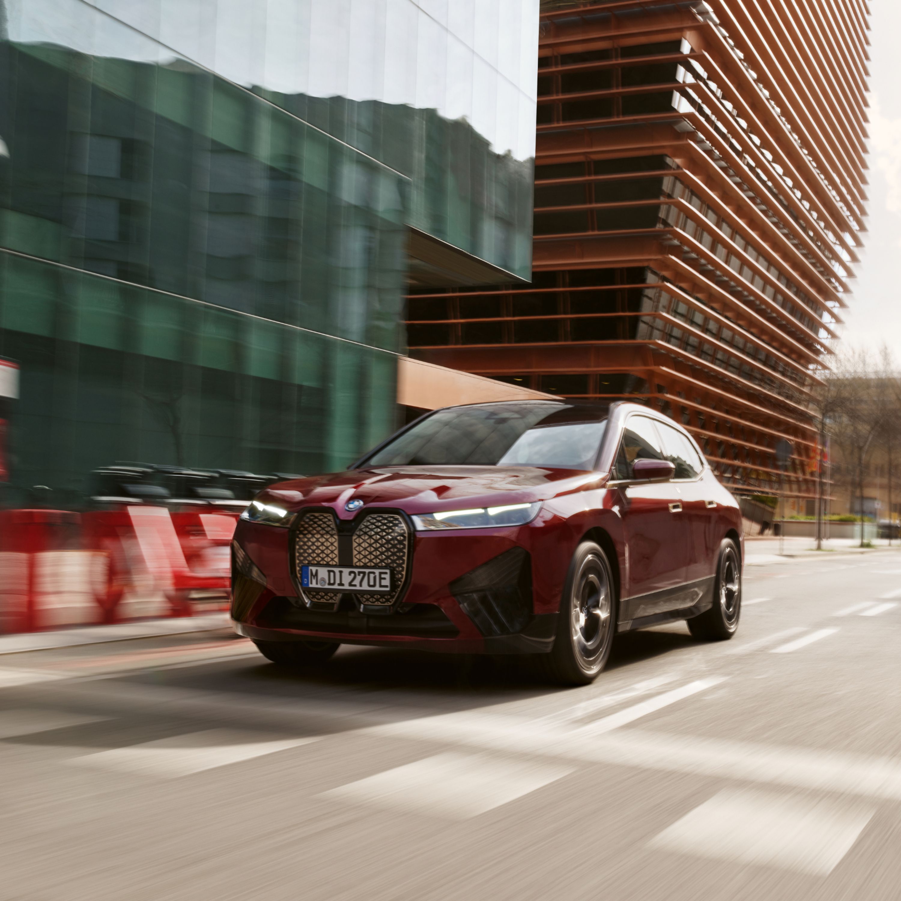 BMW iX Electric SUV in Autumn Red driving on a main street in an urban setting.