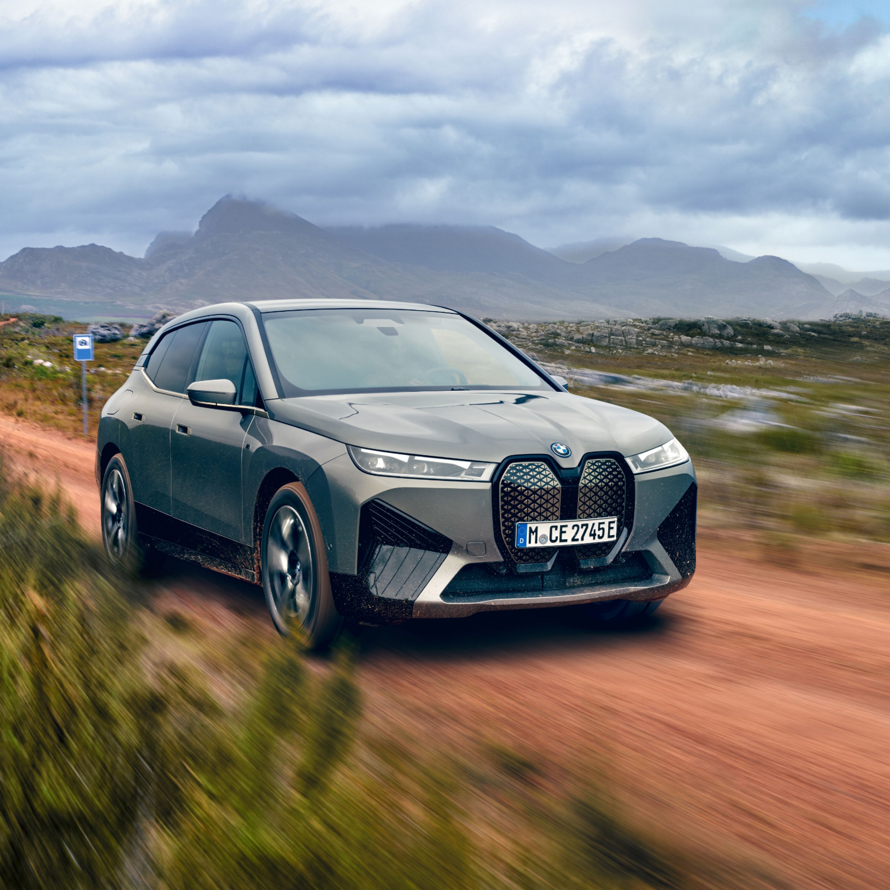 BMW iX M60 Elektro SUV in Storm Bay Metallic auf einem unwegsamen Feldweg inmitten der freien Natur fahrend