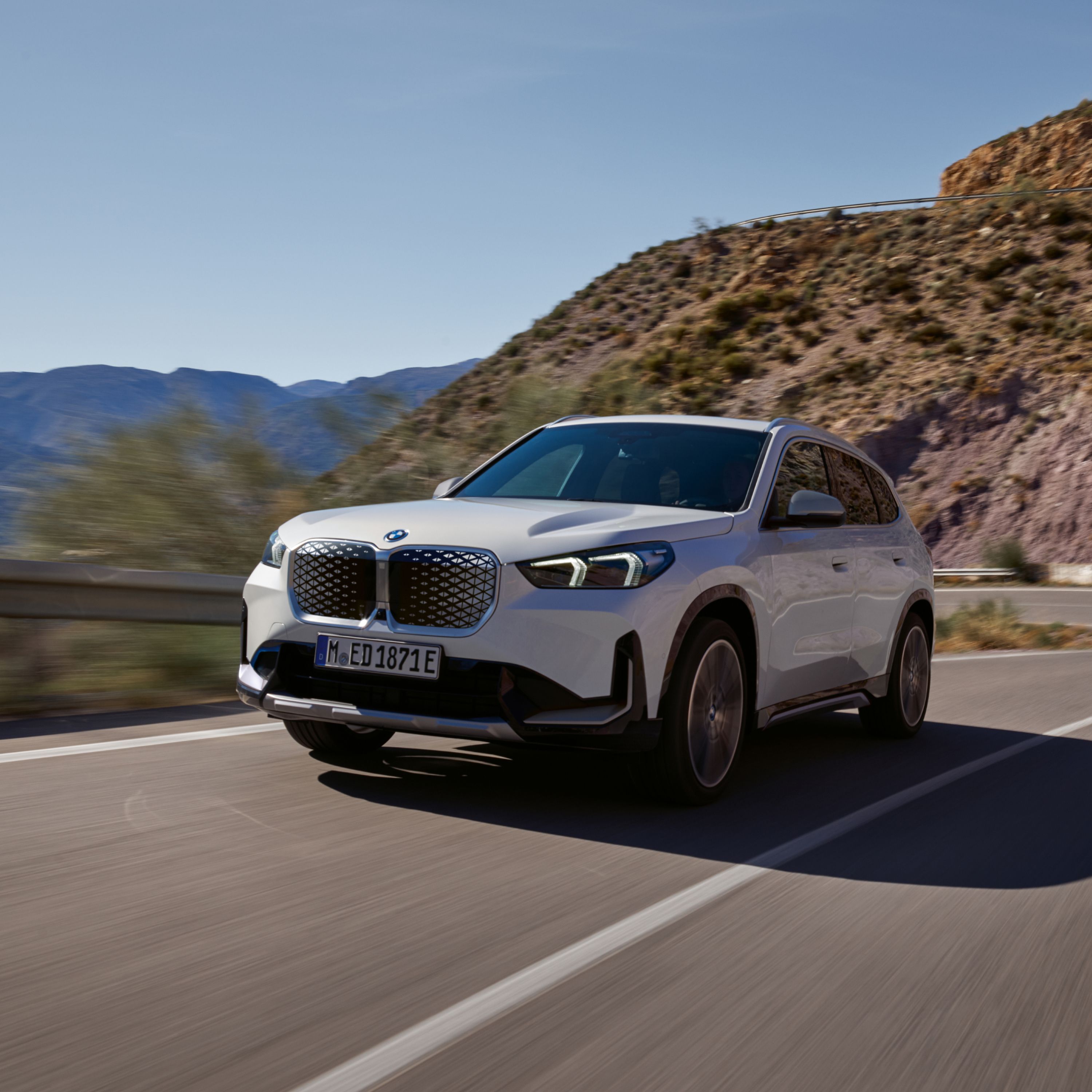 BMW iX1 Electric SUV in alpine white driving down a road through rocky mountain terrain