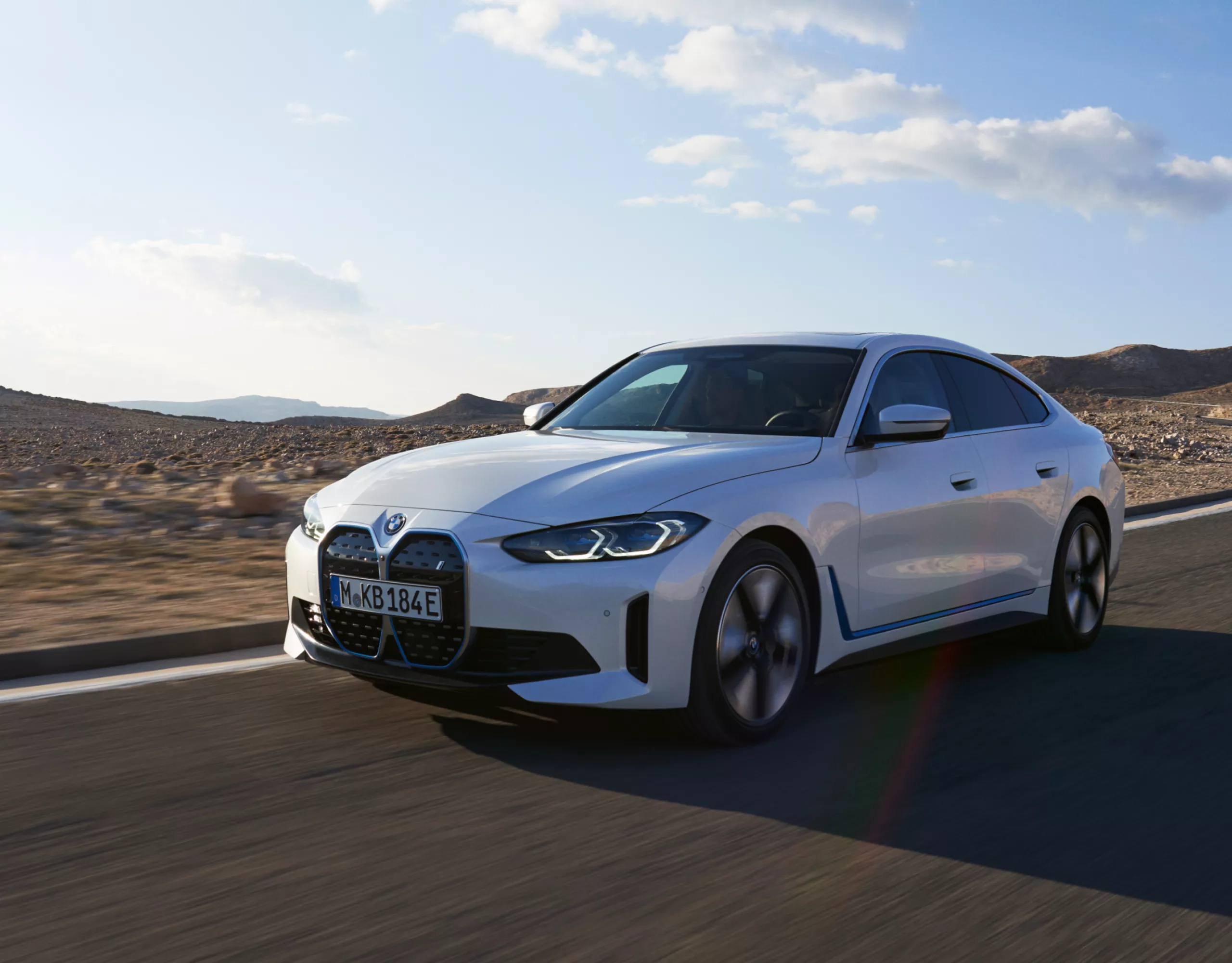 BMW i4 Gran Coupé en Tansanitblau Metallic sur une route de montagne près d'un lac avec le lever du soleil en arrière-plan