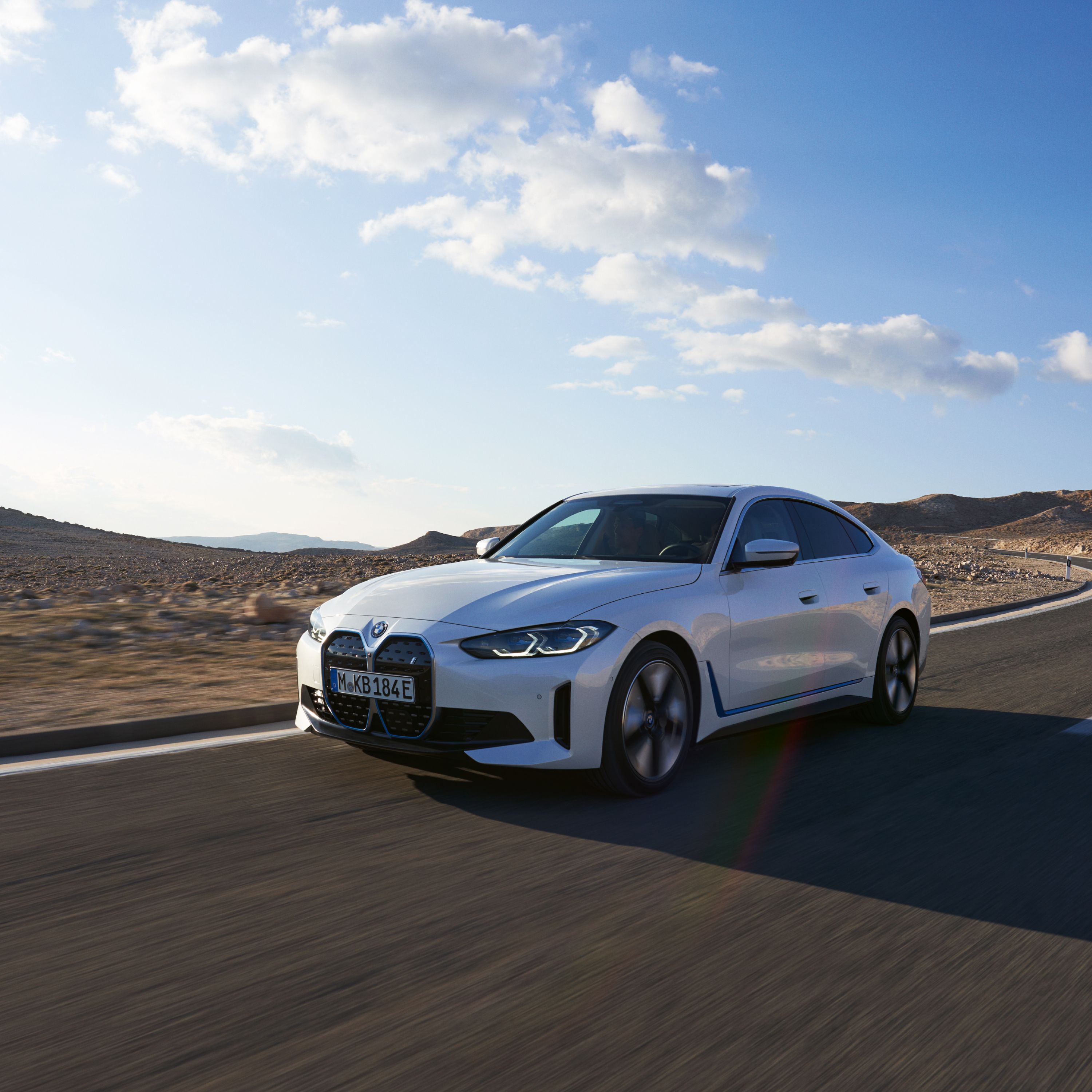 Mineralweiß Metallic BMW i4 Gran Coupé bei hoher Geschwindigkeit auf einer breiten Wüstenstraße fahrend