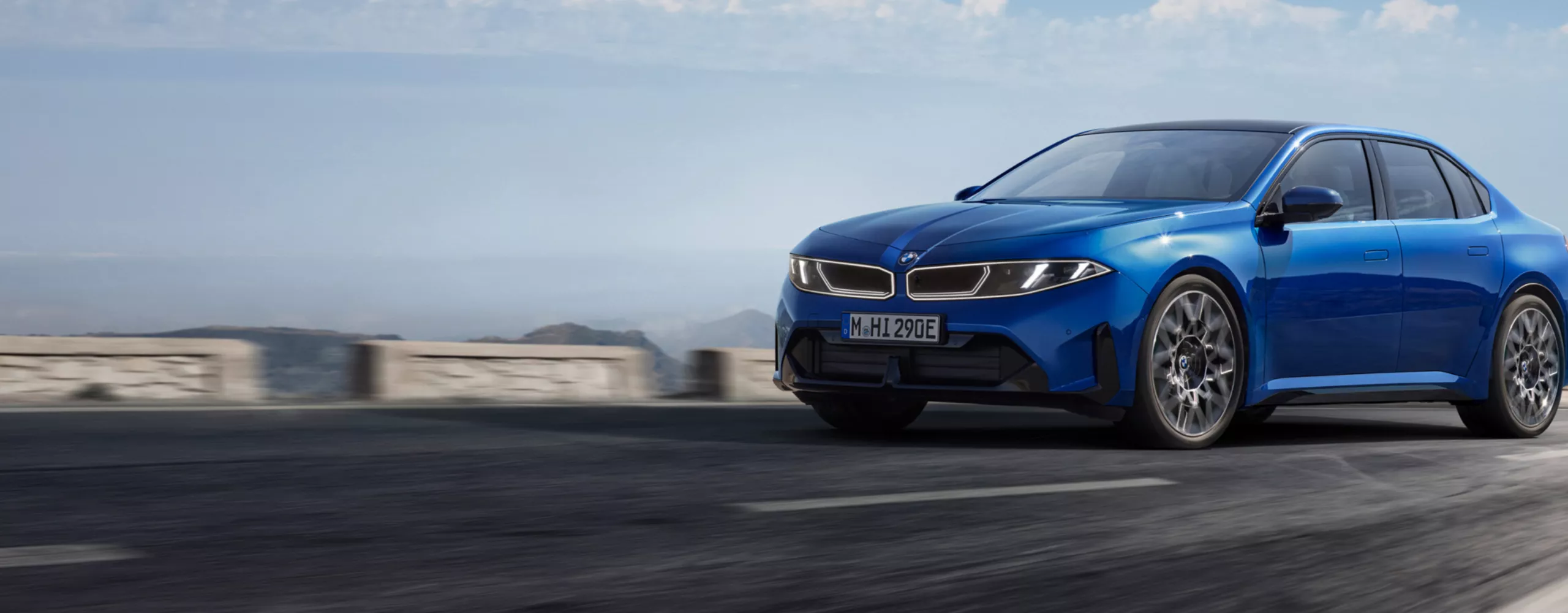 The BMW i3 Sedan drives along an urban highway through a modern city, while the vehicle is shown from various angles. The vehicle then drives along a winding road through a landscape of mountains and lakes.