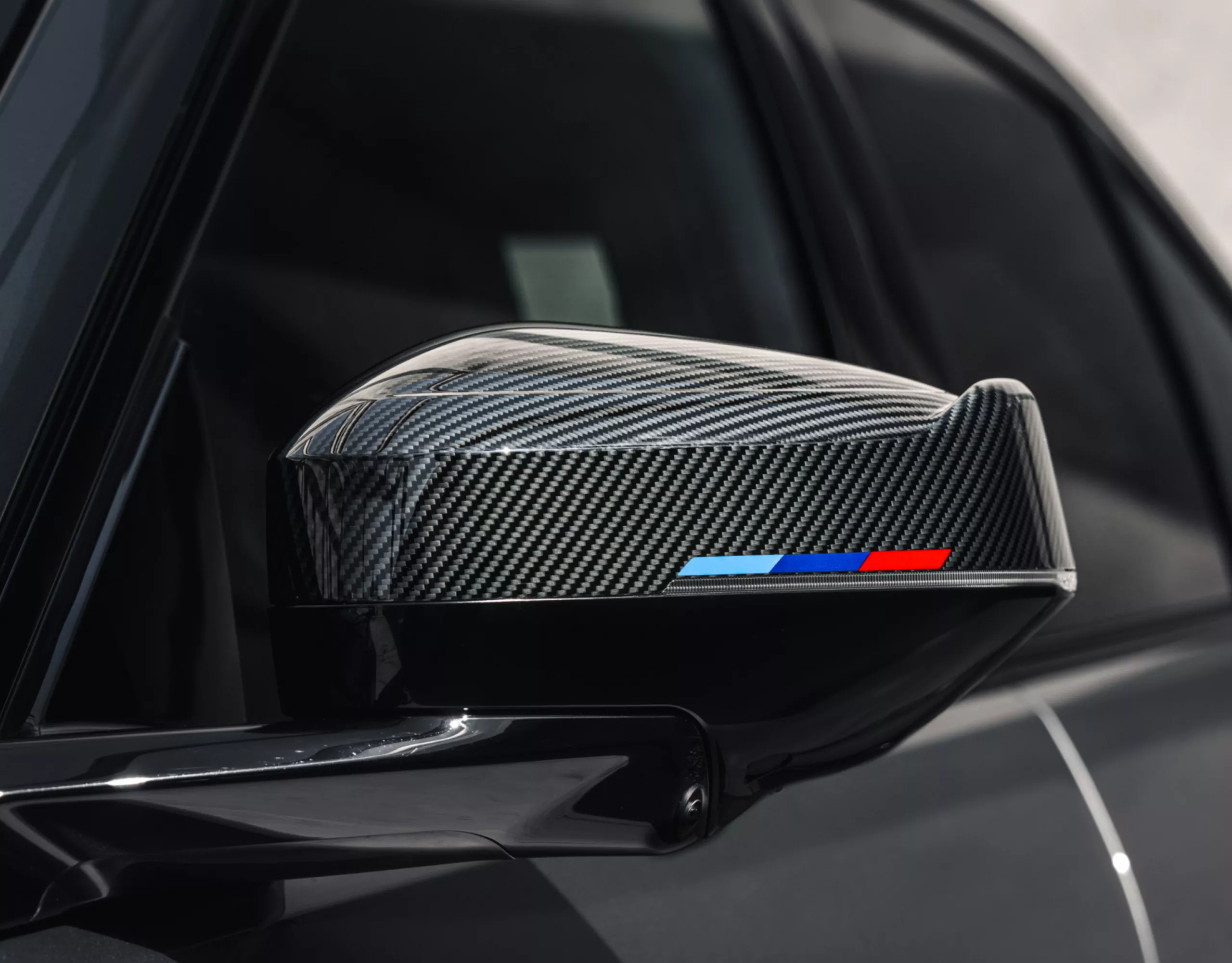 Vista detallada de una carcasa de retrovisor de los accesorios M Performance fabricada en carbono a la vista con rayas Seehaus.
