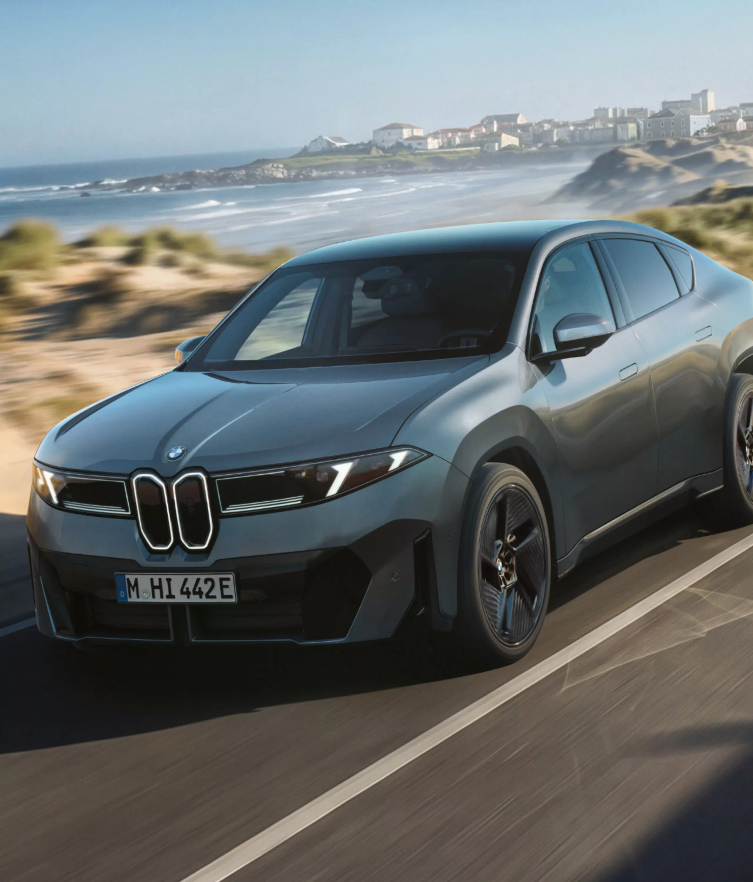 BMW iX4 50 xDrive driving on a road to demonstrate Adaptive M Suspension.