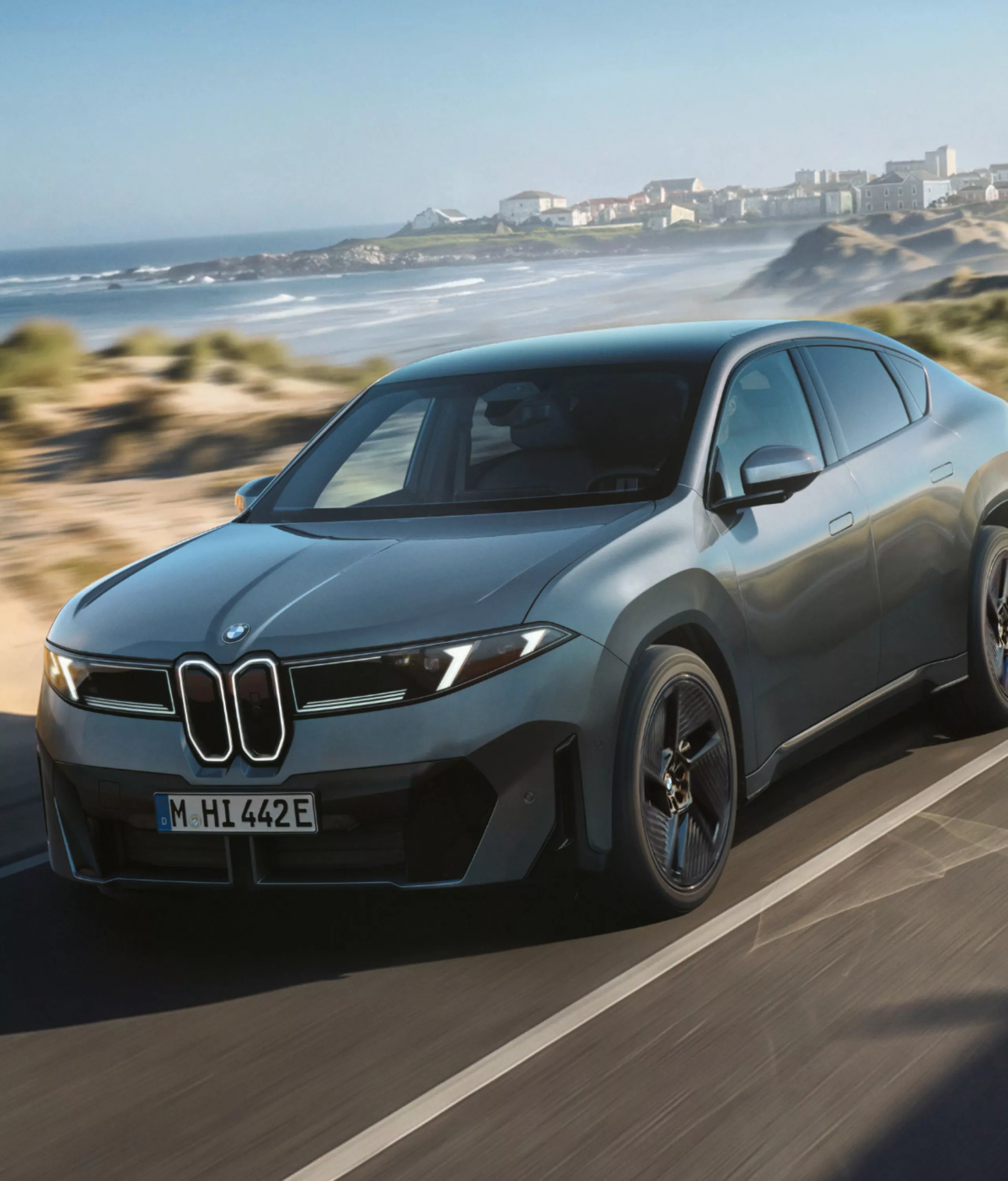 BMW iX4 50 xDrive driving on a road to demonstrate Adaptive M Suspension.