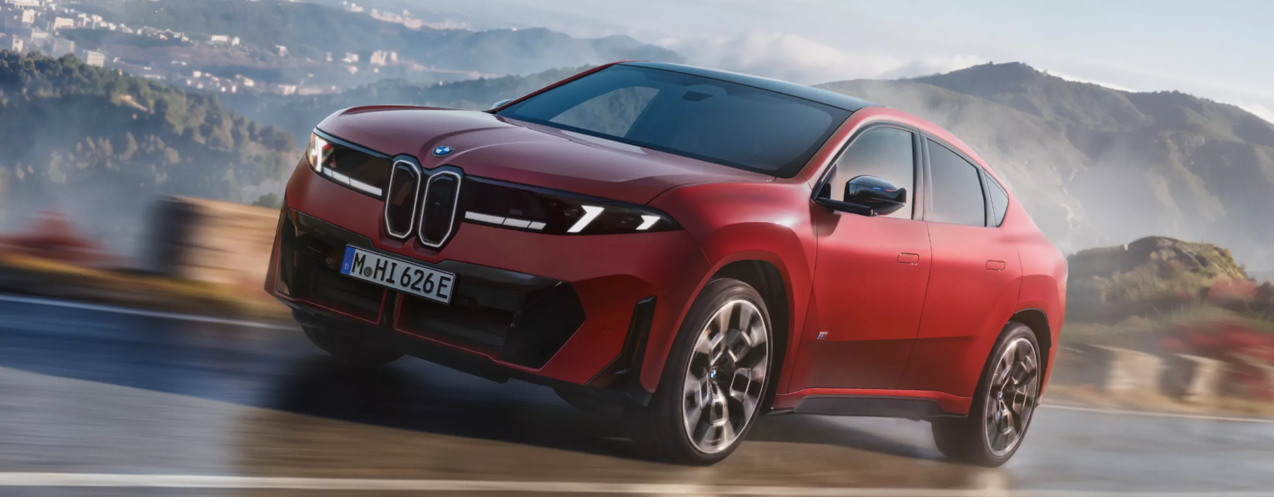 BMW iX4 M60 xDrive cornering on a winding road to demonstrate Adaptive M Suspension