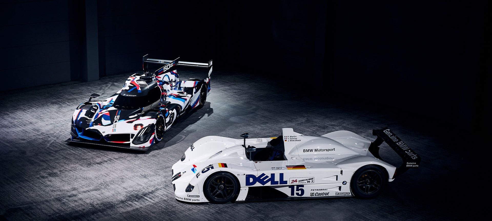 Zwei Männer in Werkstatt-Overalls heben die Motorhaube eines BMW an. Im Hintergrund ist ein abgedecktes Auto zu sehen